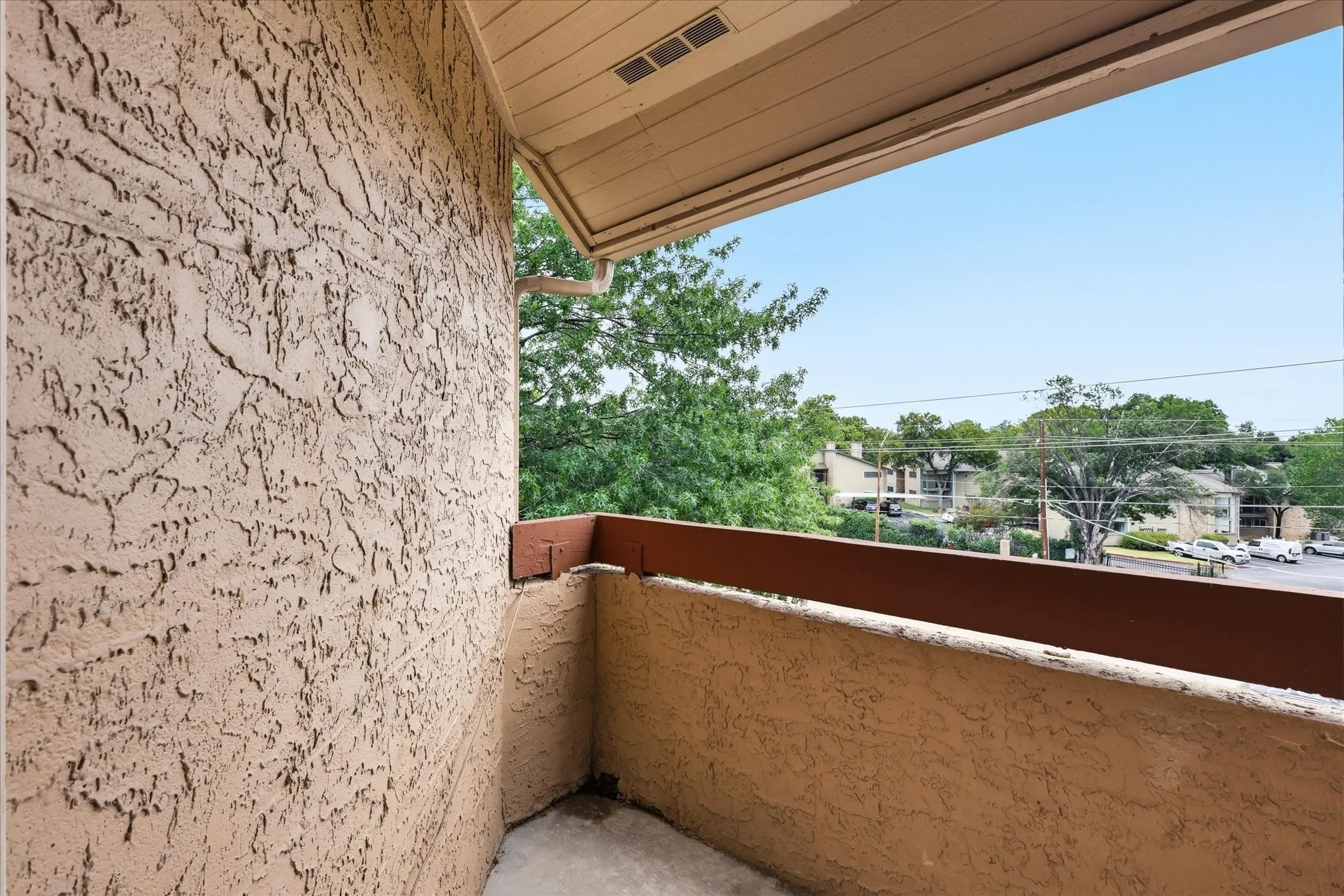 Private outdoor balcony with textured stucco walls, wood-finish railing, and a clear sky overhead