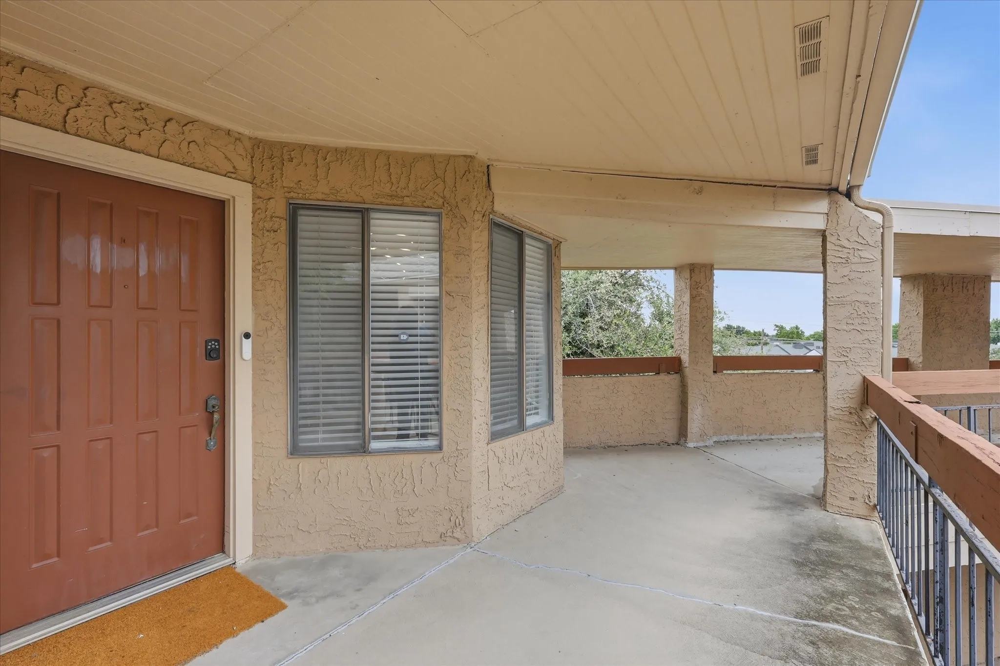 Covered outdoor patio with textured stucco walls, a paneled entry door, and integrated window blinds