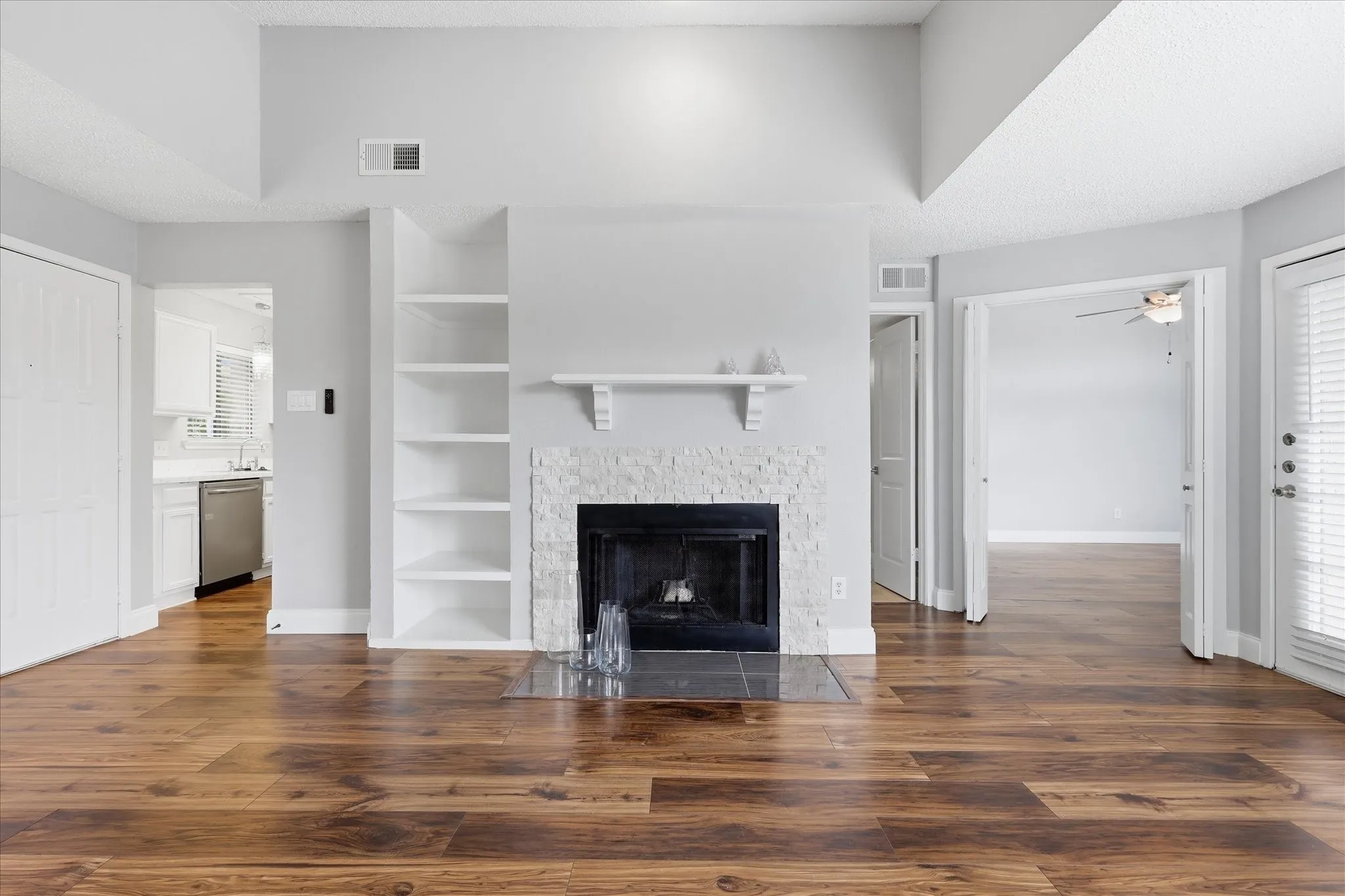 Living area featuring a fireplace with a textured stone surround, wood-finish flooring, and built-in shelving