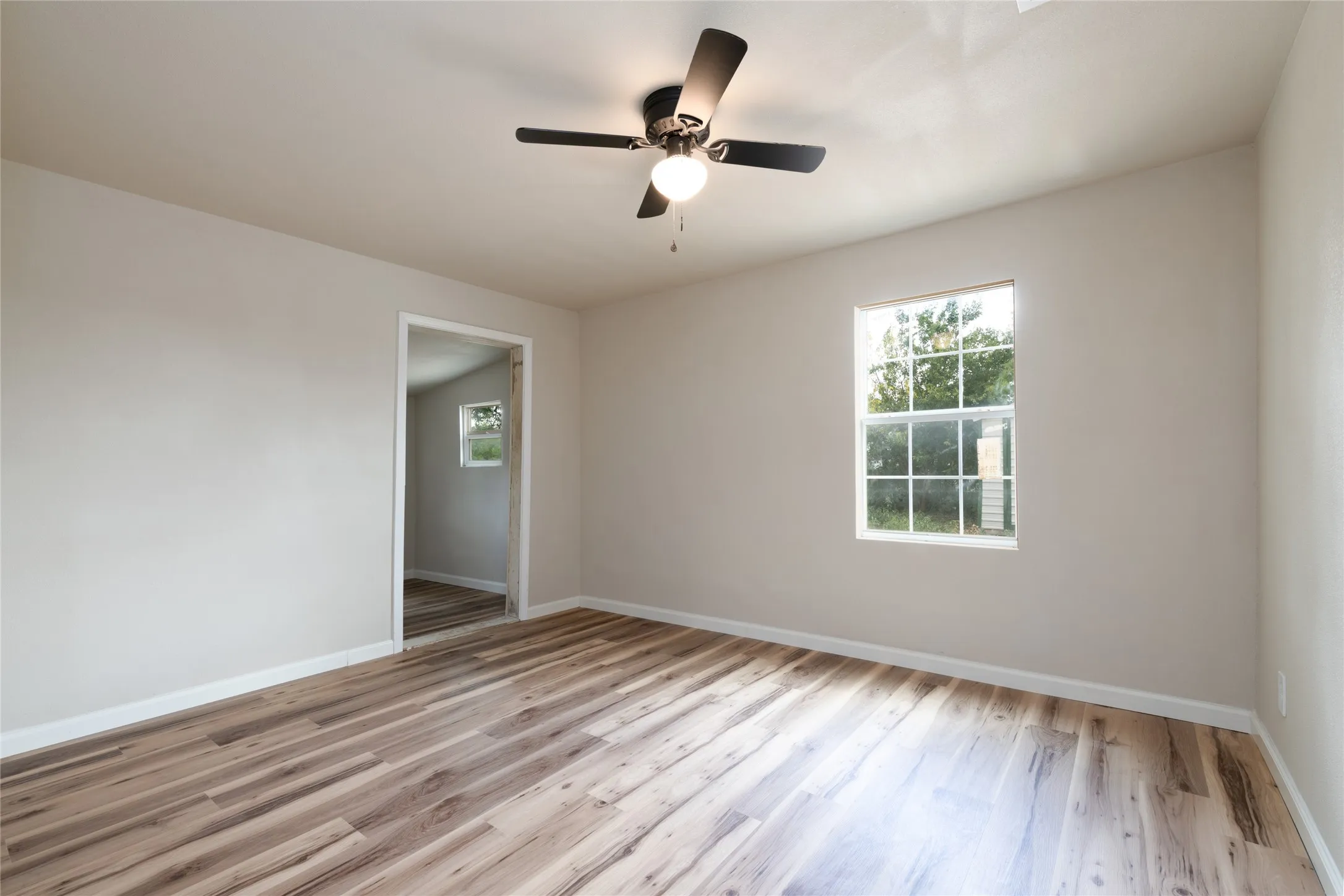 Interior room featuring wood-finish flooring, light-toned wall paint, a ceiling fan with integrated lighting, and a white-framed window