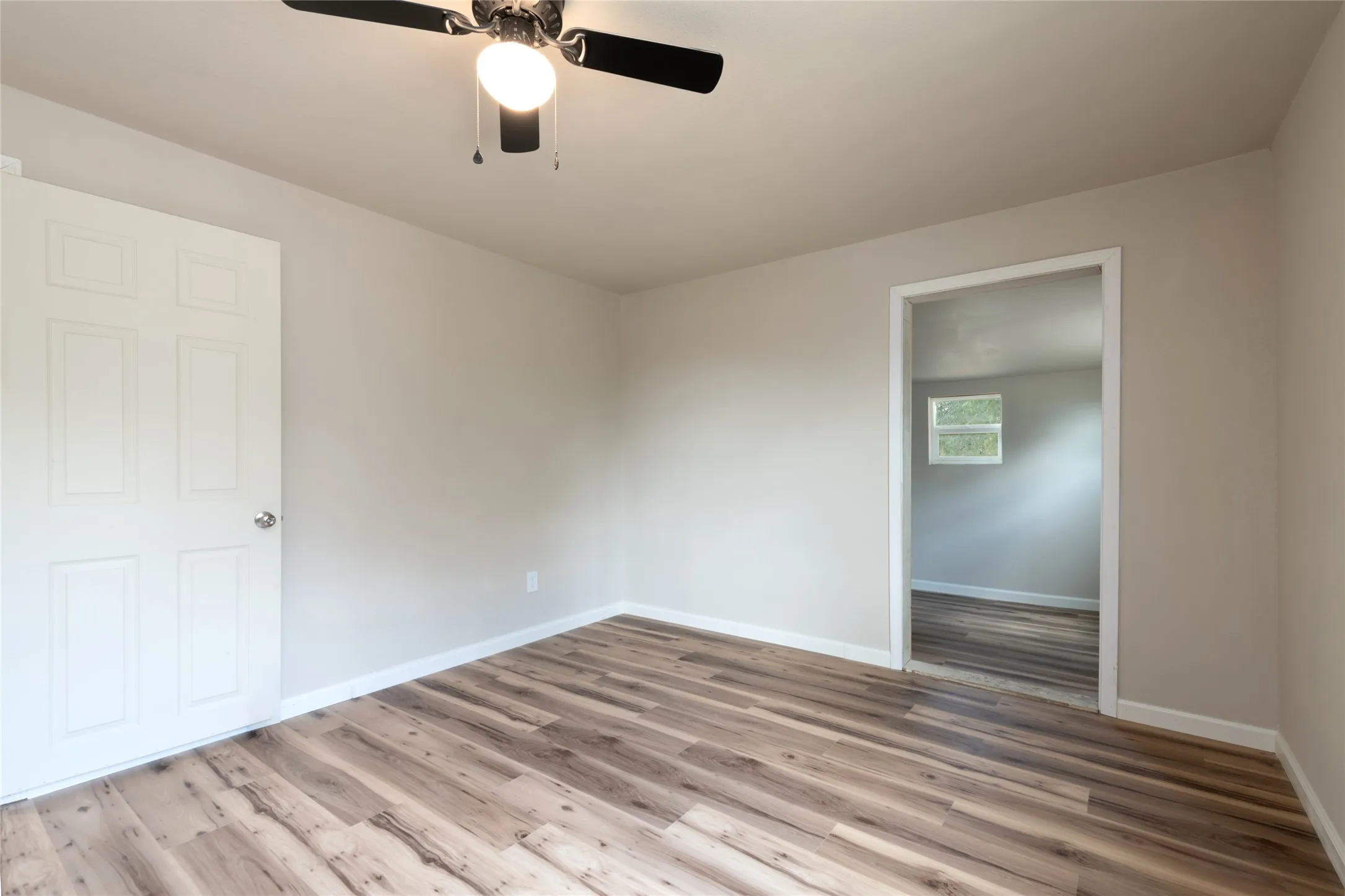 Spacious room featuring wood-finish flooring, light neutral wall paint, and a ceiling fan with integrated lighting