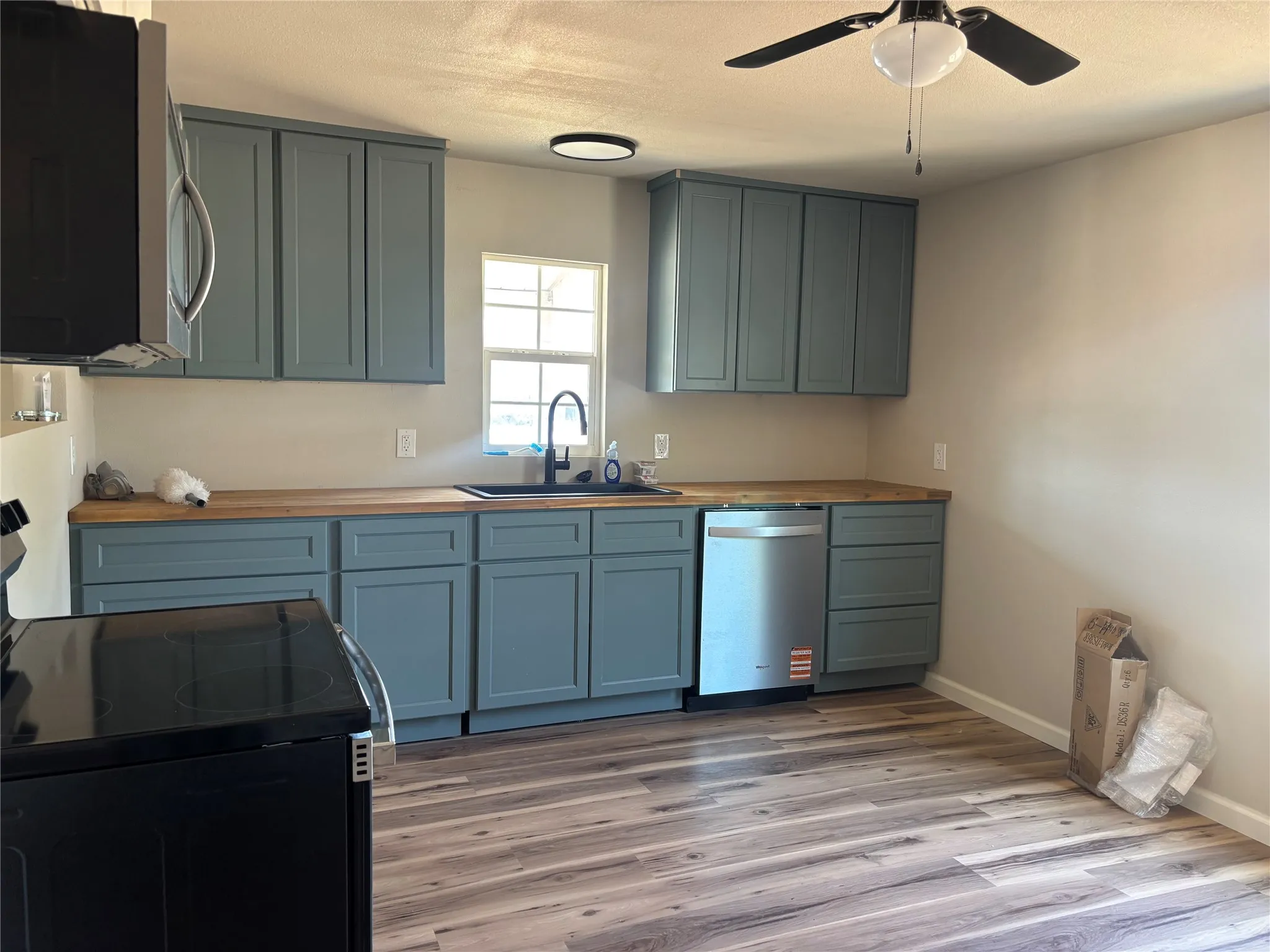 Kitchen featuring wood-finish flooring, teal cabinetry, wood countertops, and a stainless steel dishwasher
