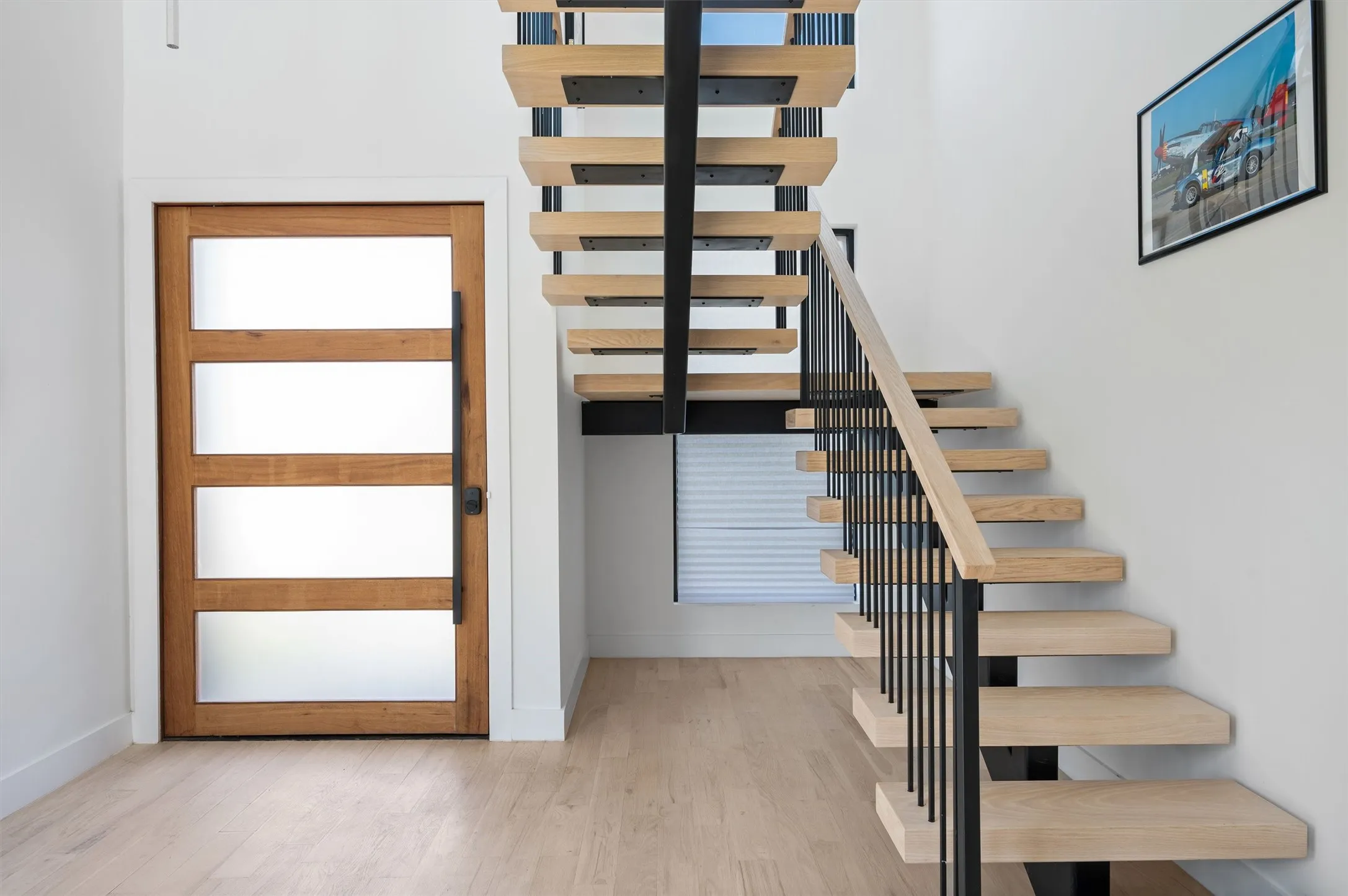 Floating White Oak Staircase Creates A Stunning Architectural Focal Point, Complemented By Sleek Steel Railings, Wide-Plank Hardwood Floors, And A Contemporary Glass Front Door.