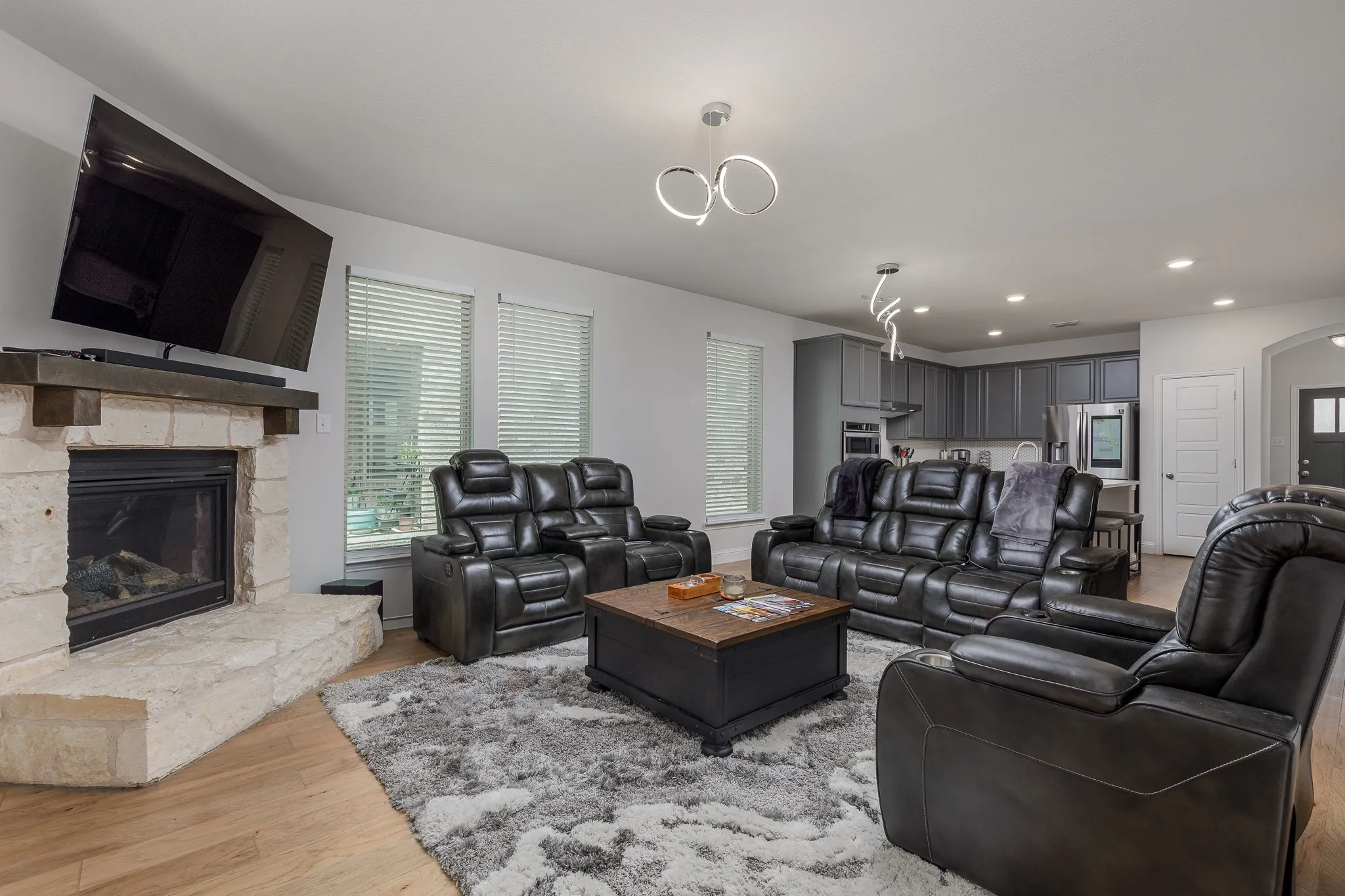 Open-concept living space featuring a stone-clad fireplace with a substantial wood mantel, wood-finish flooring, and recessed lighting