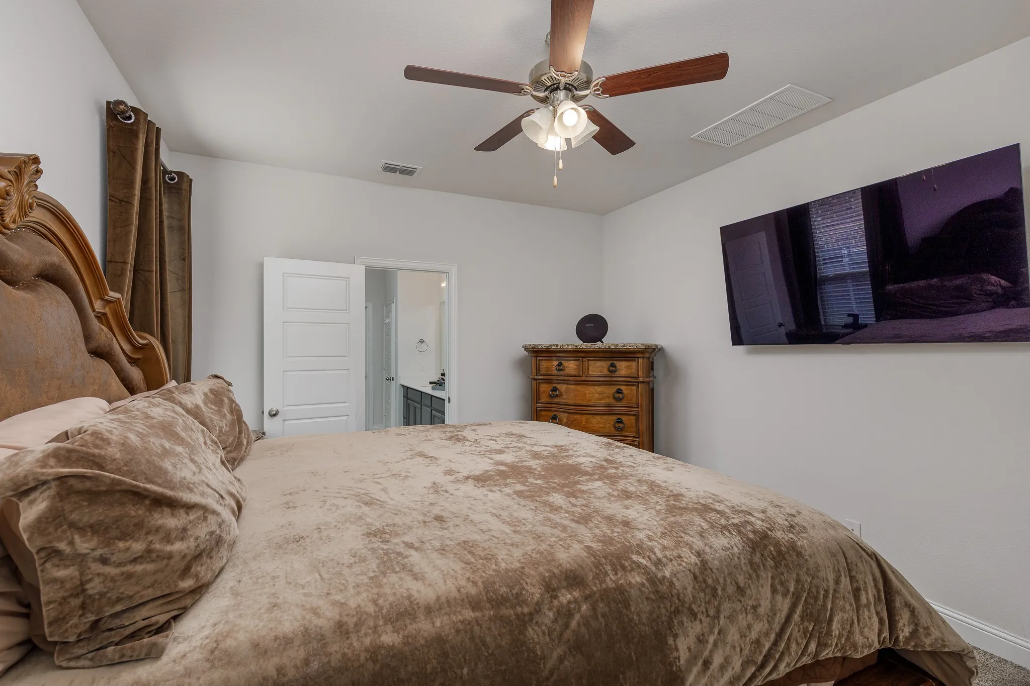 Bedroom featuring a ceiling fan with integrated lighting, a paneled door, and a wall-mounted ventilation register