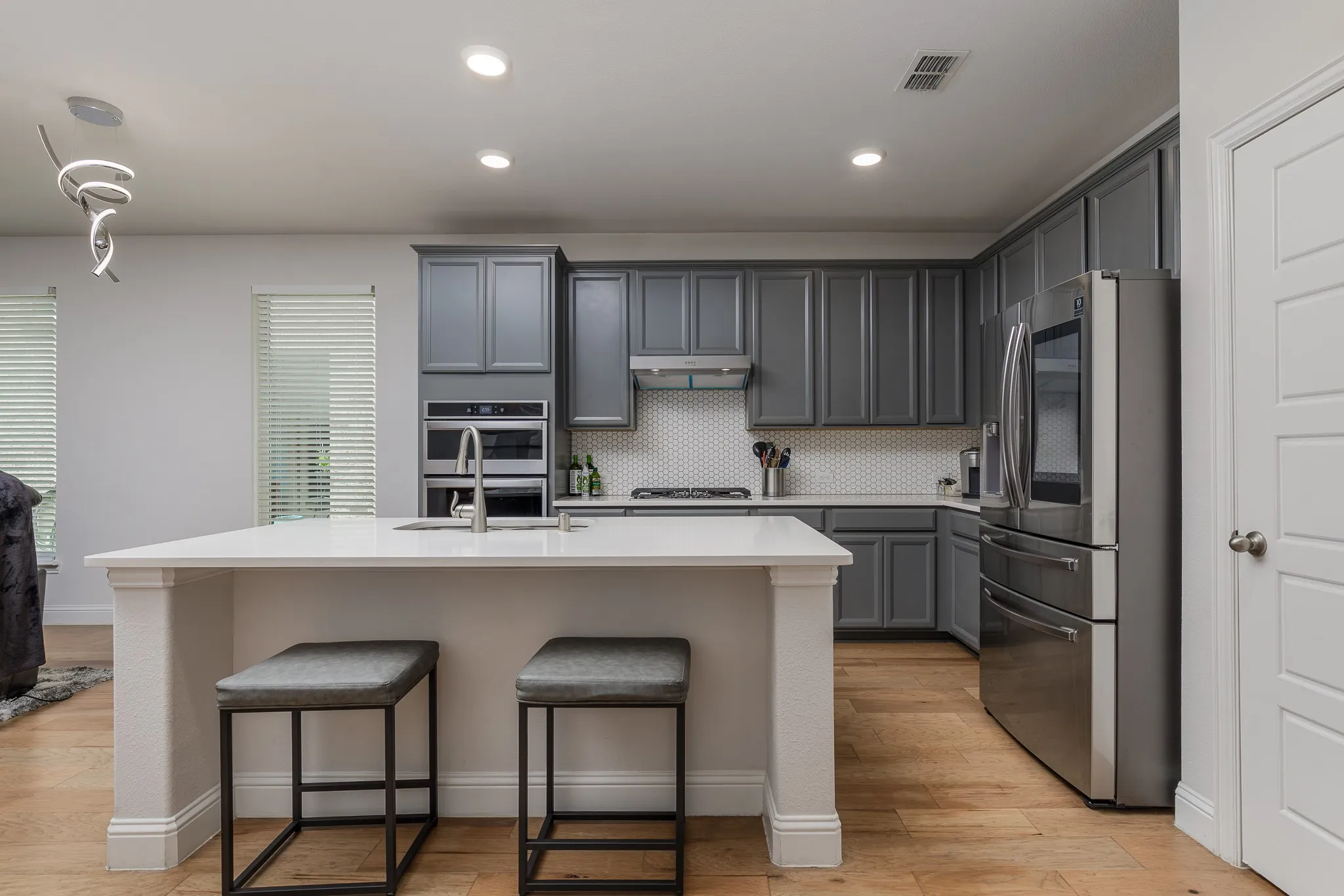 Modern kitchen featuring gray cabinetry, stainless steel appliances, white hexagon tile backsplash, and wood-finish flooring