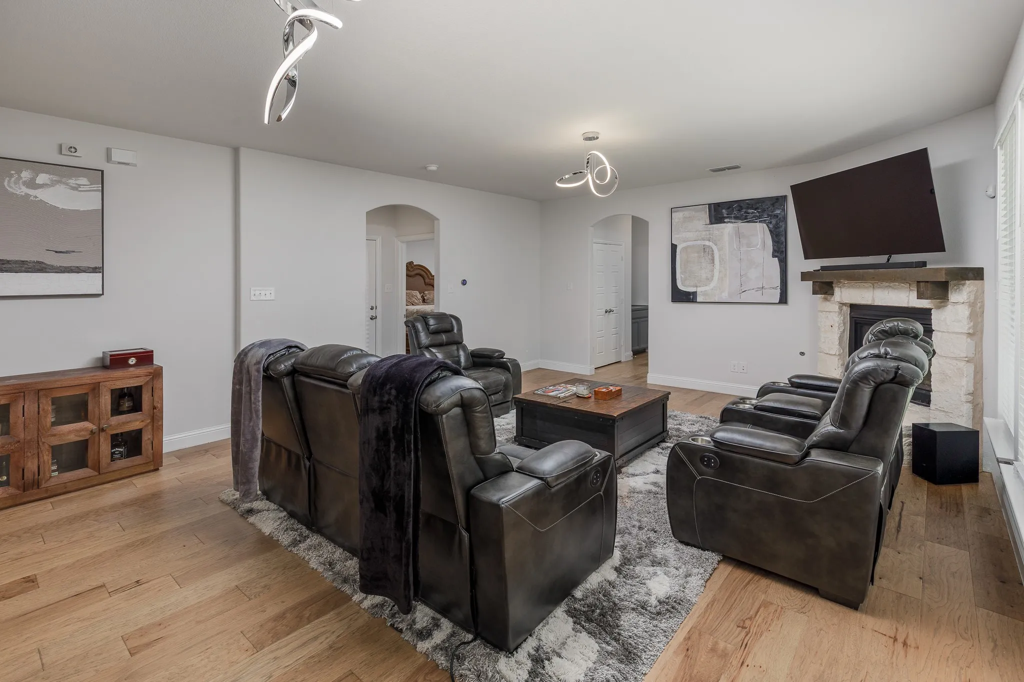 Living area featuring wood-finish flooring, a stone fireplace with a substantial wood mantle, and white walls