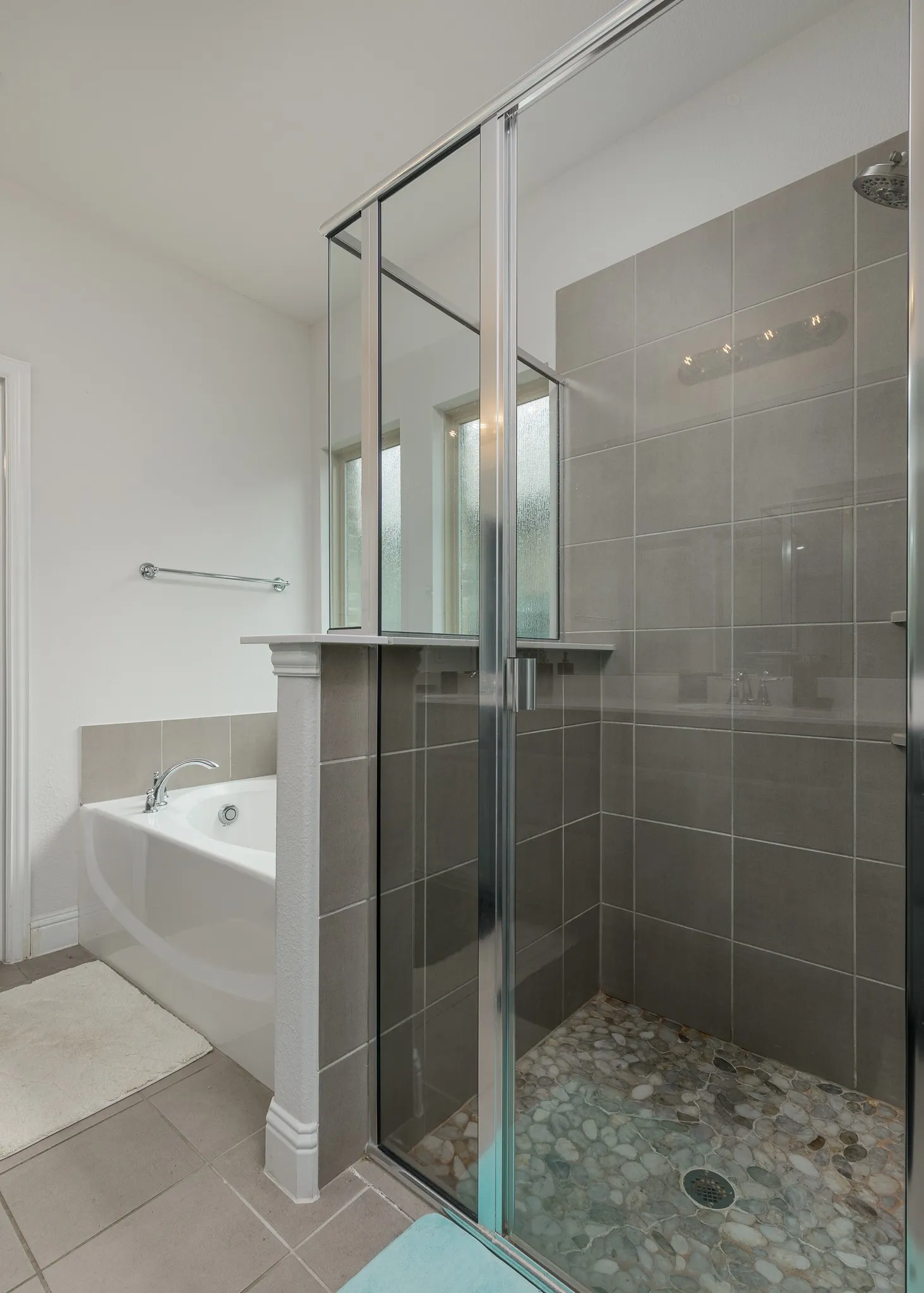 Glass-enclosed shower with pebble-finish flooring and gray wall tiling
