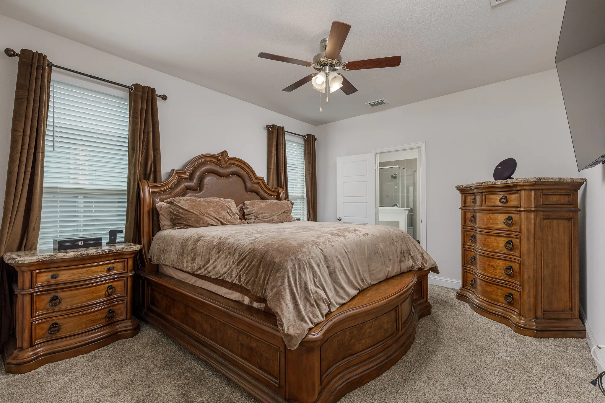 Carpeted room featuring a ceiling fan with integrated lighting, two windows with blinds and drapes, and a white interior door
