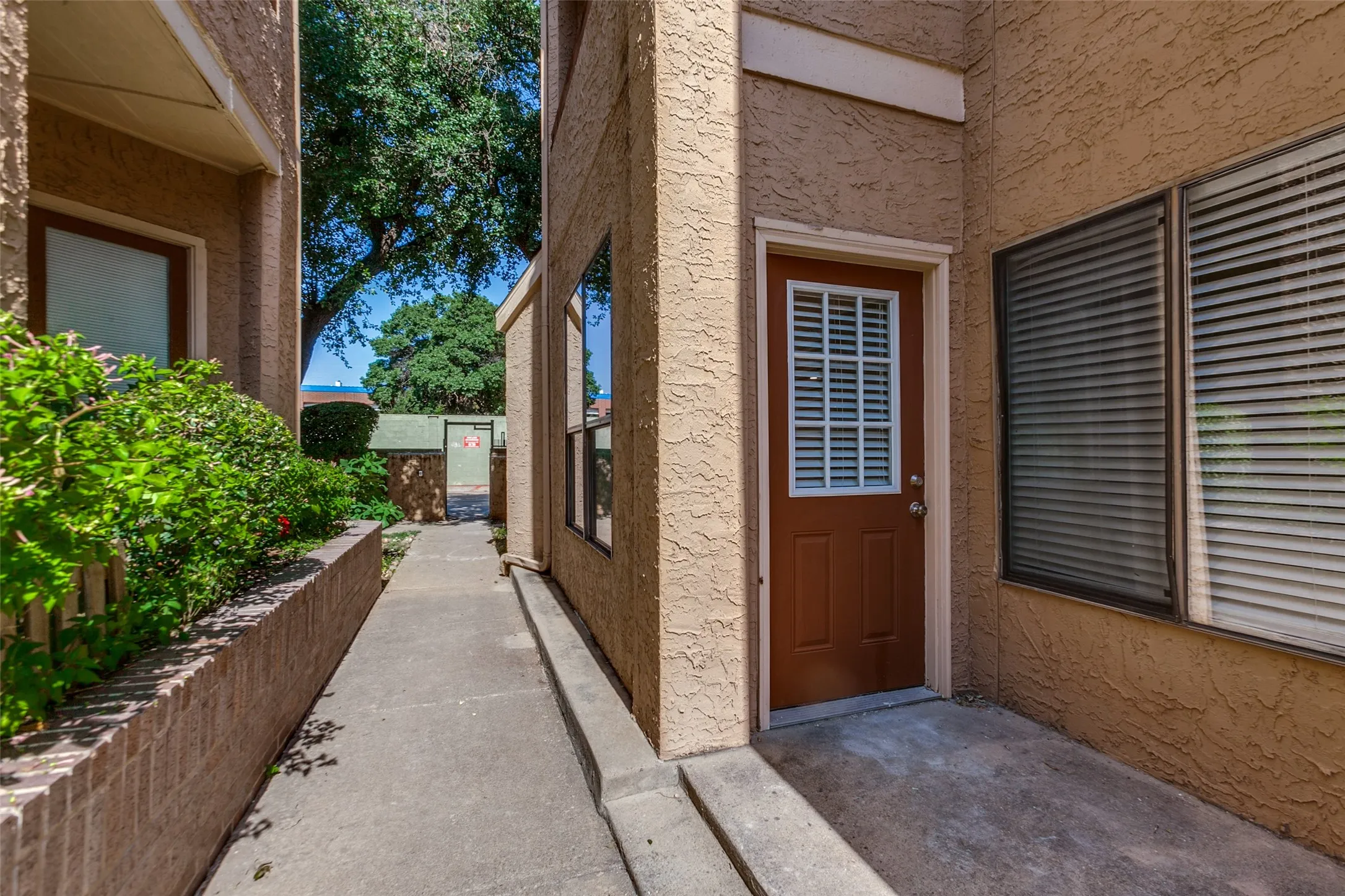 Brown entry door with a white louvered window, textured stucco exterior, and concrete walkway