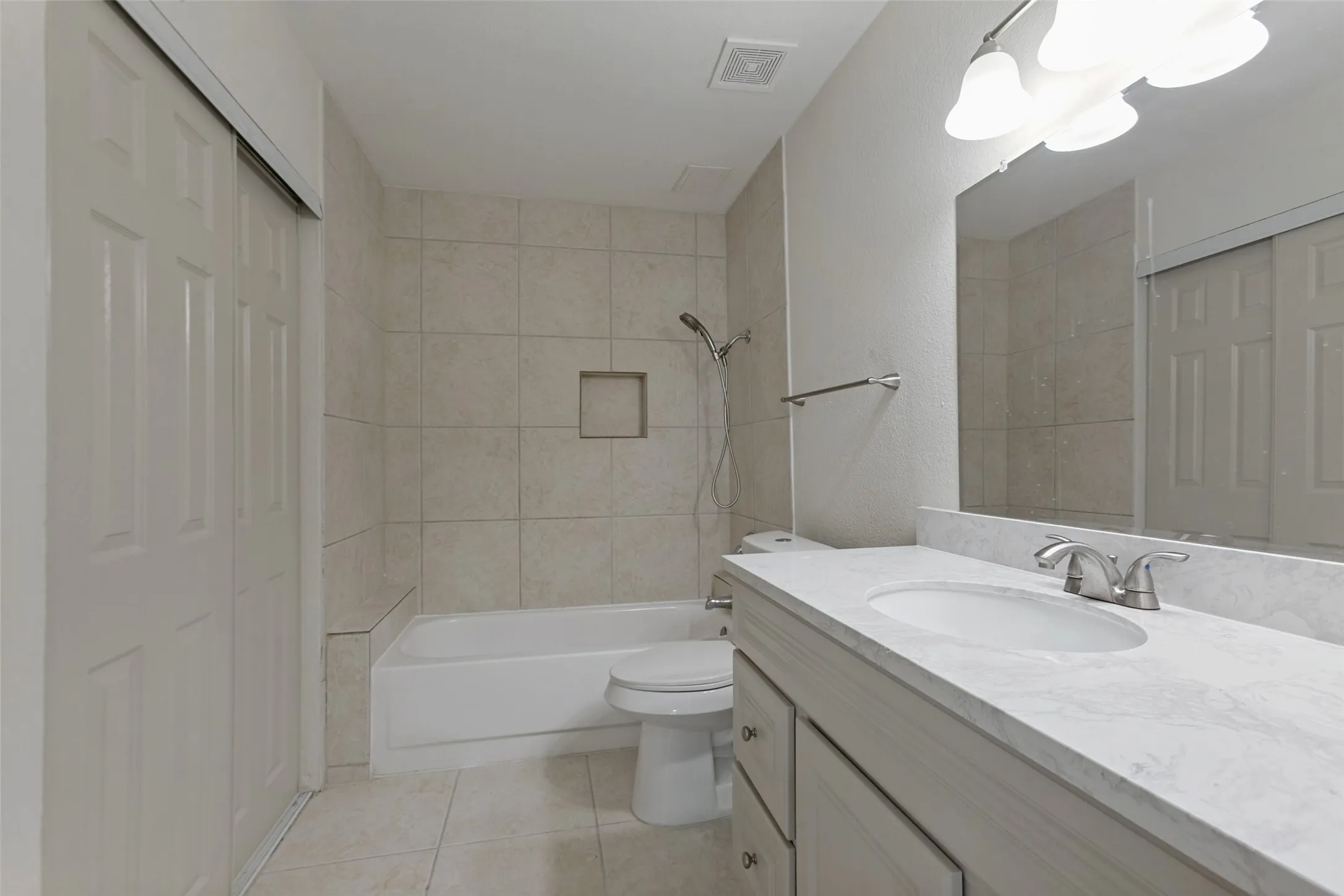 Bathroom featuring a vanity with an integrated sink, a large mirror, a shower/tub combination with tiled surround, and tile flooring