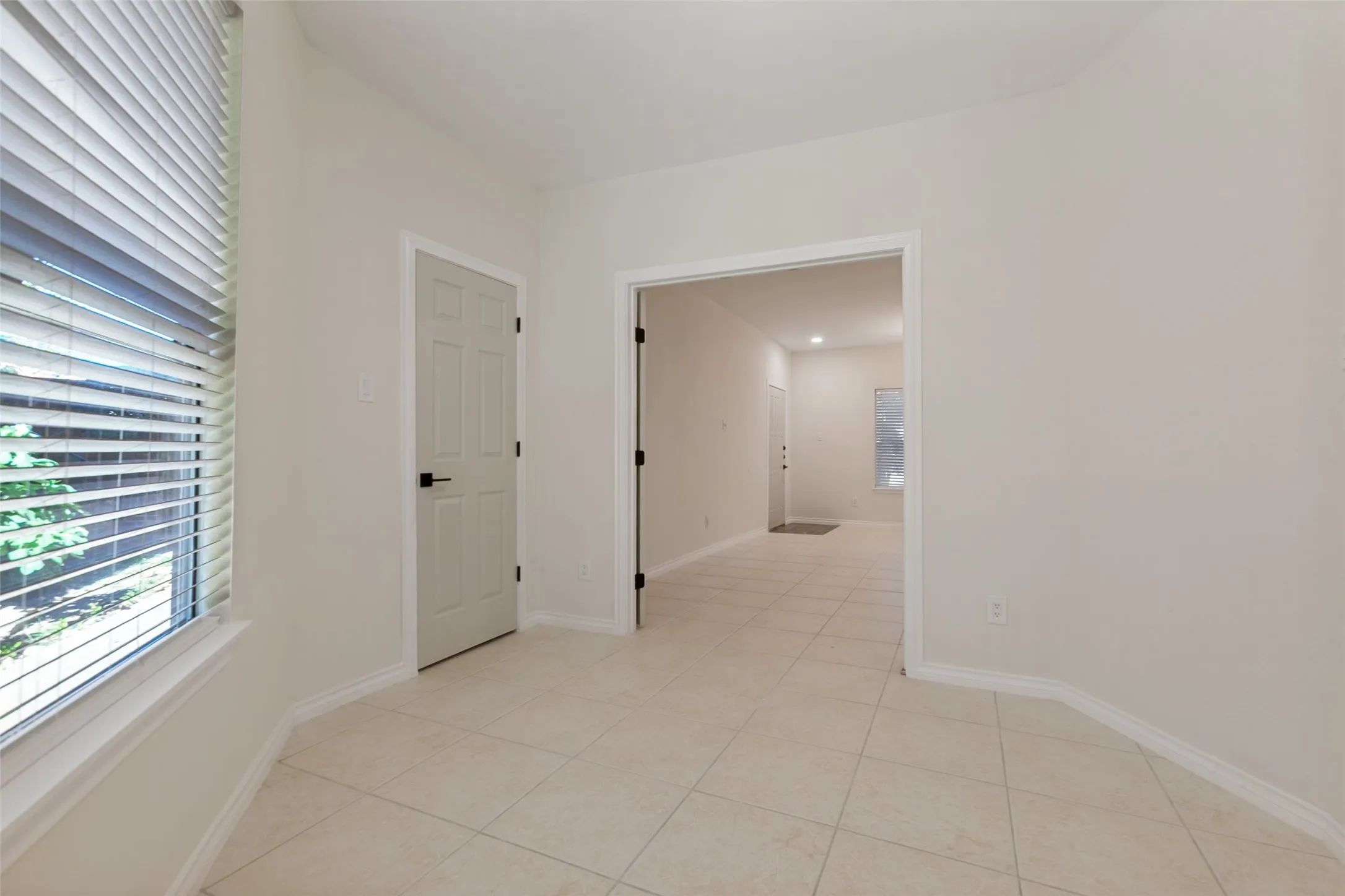 Room featuring light tile flooring, a window with horizontal blinds, a six-panel door with black hardware, and an open doorway leading to an interior space
