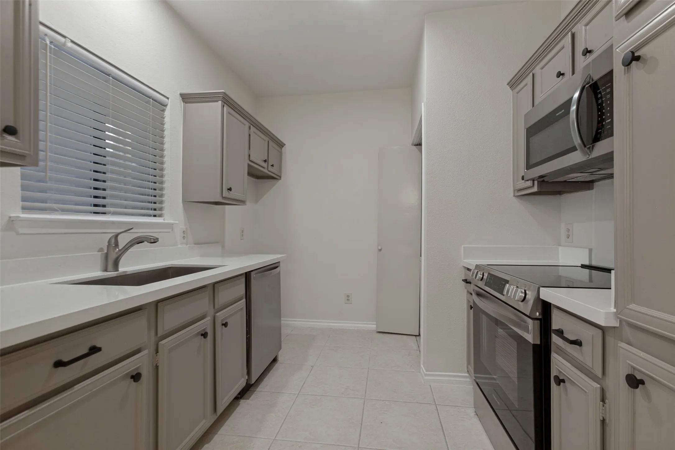 Contemporary kitchen featuring light gray cabinetry with black hardware, white countertops, stainless steel appliances, and tiled flooring