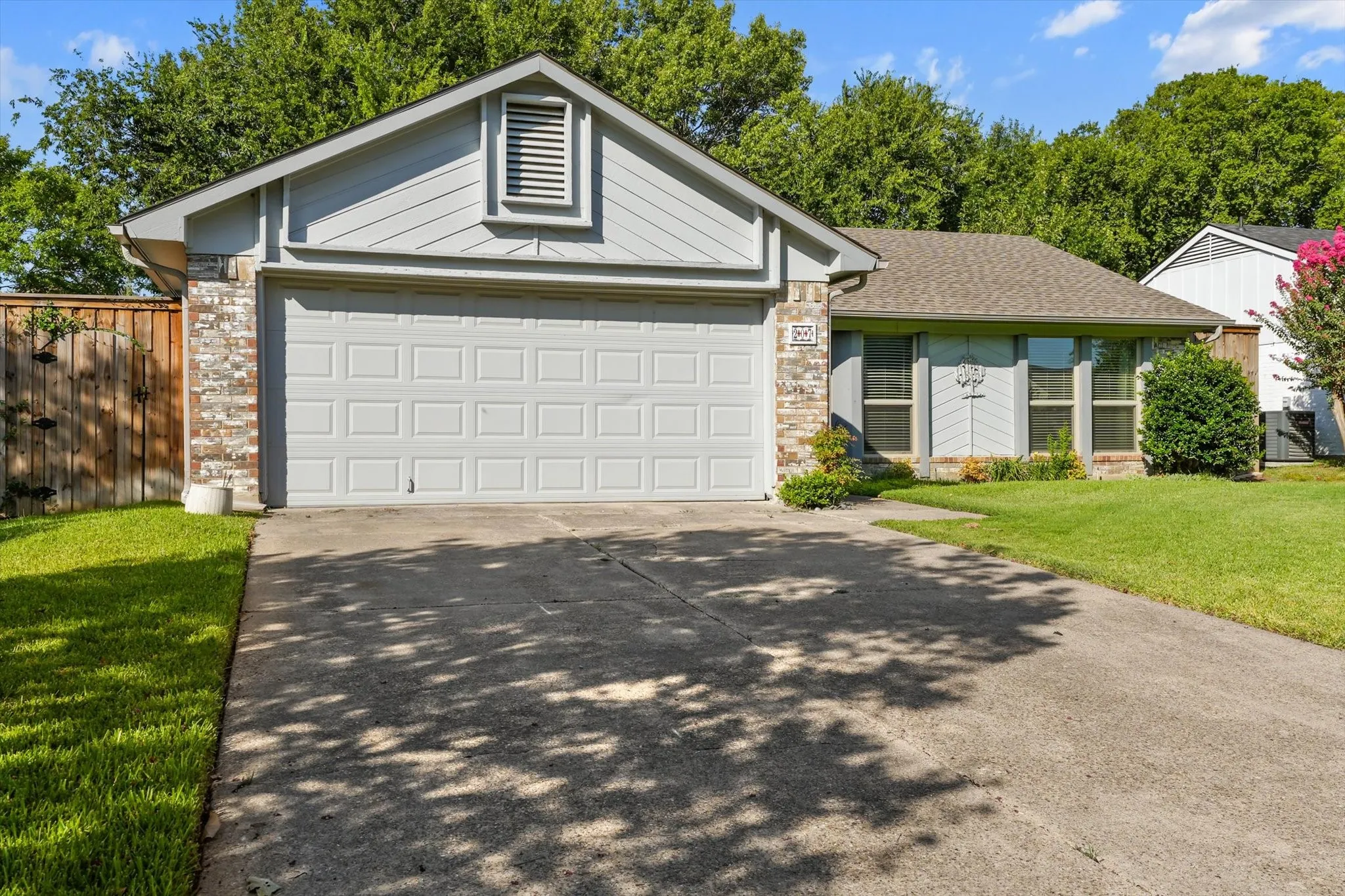 Front exterior with a shingled roof, brick accents, horizontal siding, an attached garage and mature trees.