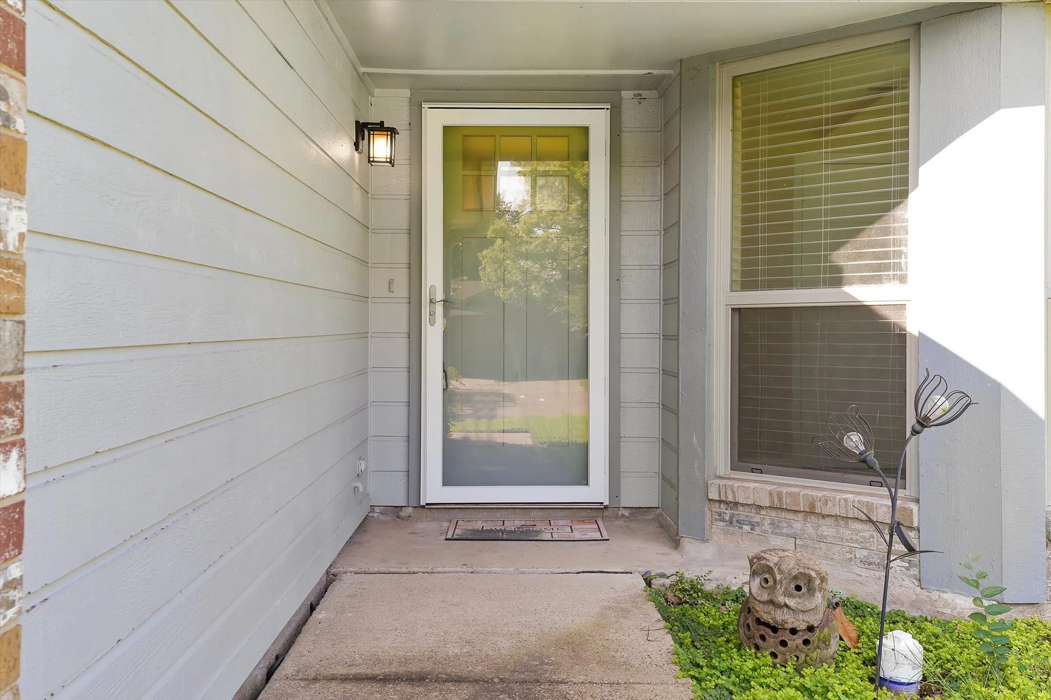 Concrete walkway leading to a full-light storm door, flanked by horizontal siding and a brick facade