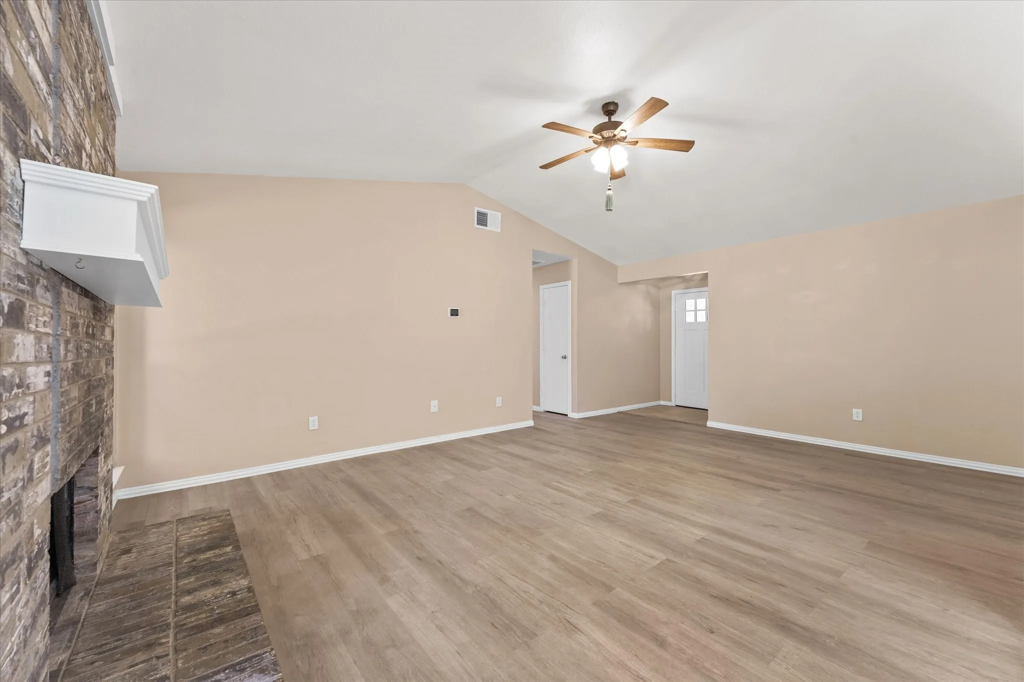 Vaulted ceiling with a ceiling fan, brick wood burning fireplace with a white mantel, wood-finish LVP flooring, and light-colored walls