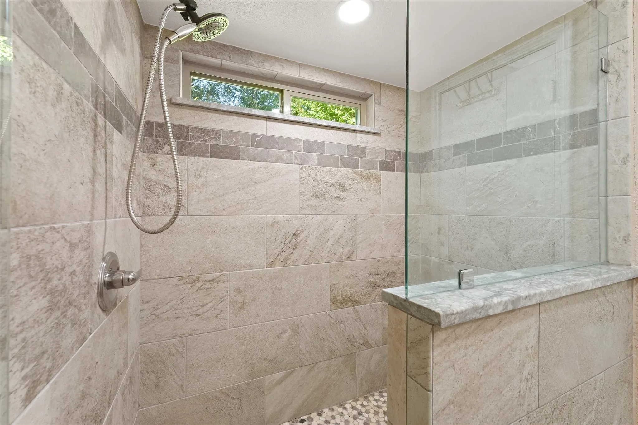 Shower featuring floor-to-ceiling tile, a glass enclosure, a handheld shower fixture, and a window