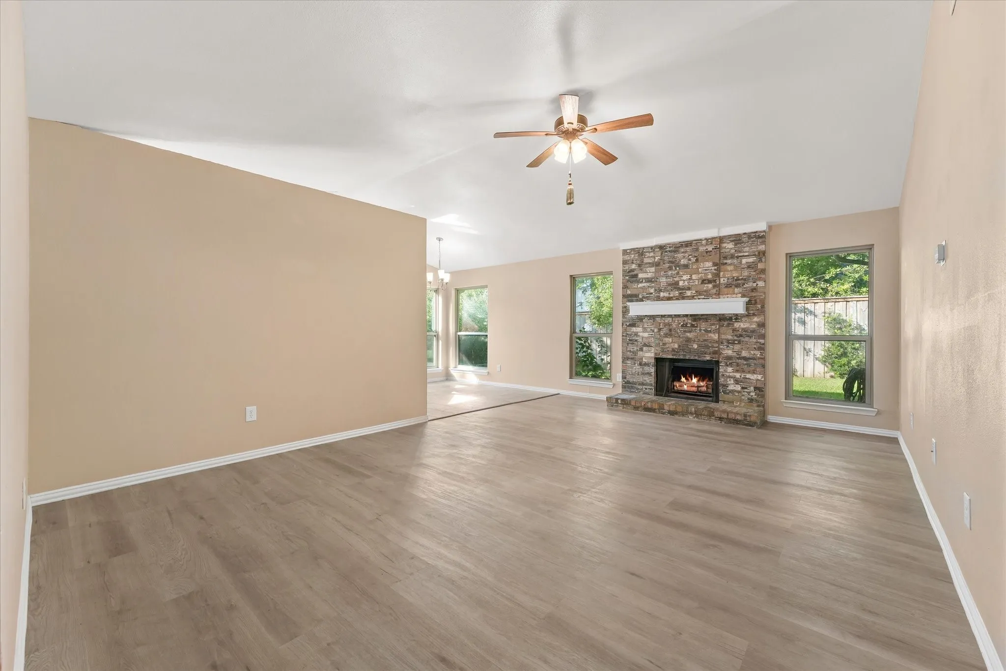 Expansive living area with wood-finish LVP flooring, a stone-clad wood burning fireplace with mantel, multiple new energy efficient windows brings in natural light, and a ceiling fan