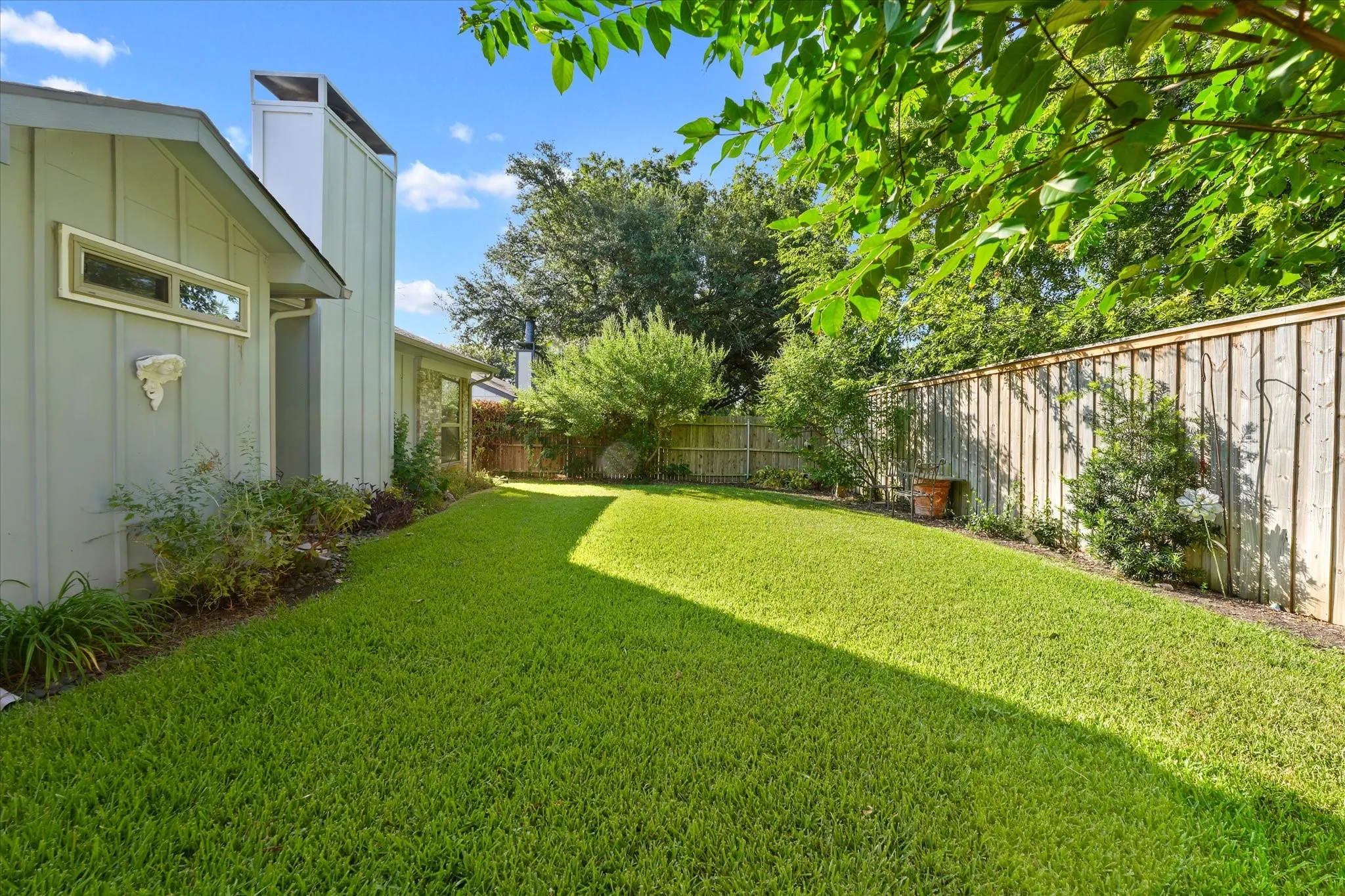 Expansive peaceful serene backyard featuring a manicured lawn, mature trees, and privacy fencing