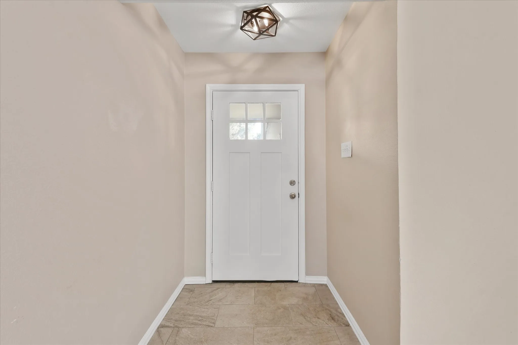 Welcoming entryway with a white six-panel entry door featuring multiple glass panes, tile flooring, and soft neutral wall finishes
