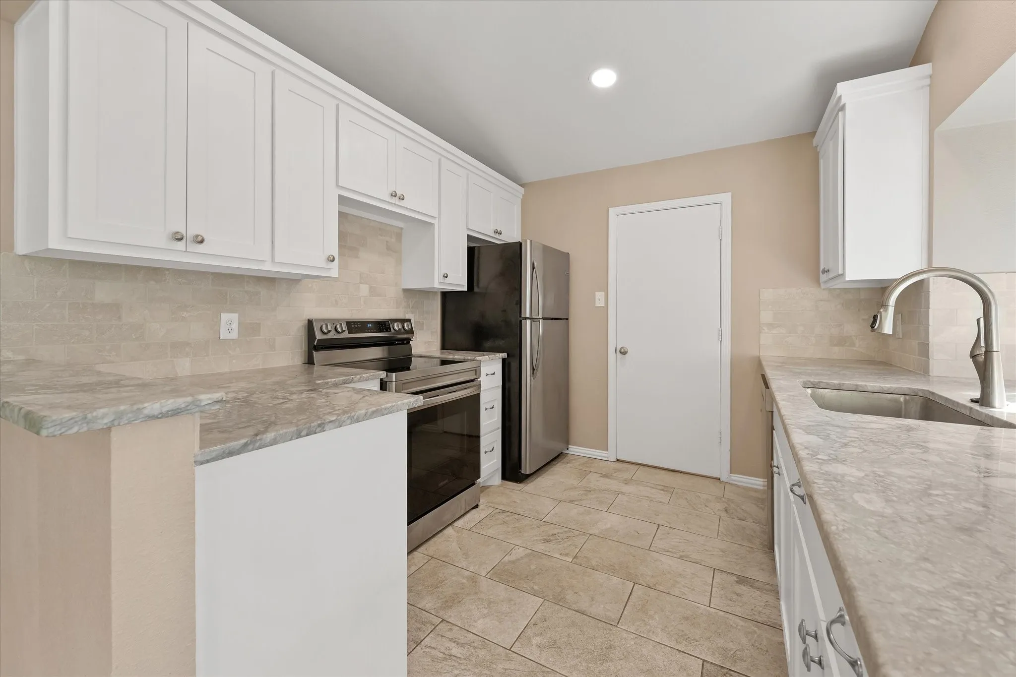 Updated white cabinetry with brushed nickel hardware, quartz countertops, stone tile backsplash, stainless steel sink with gooseneck faucet, LED recessed lighting and tile flooring
