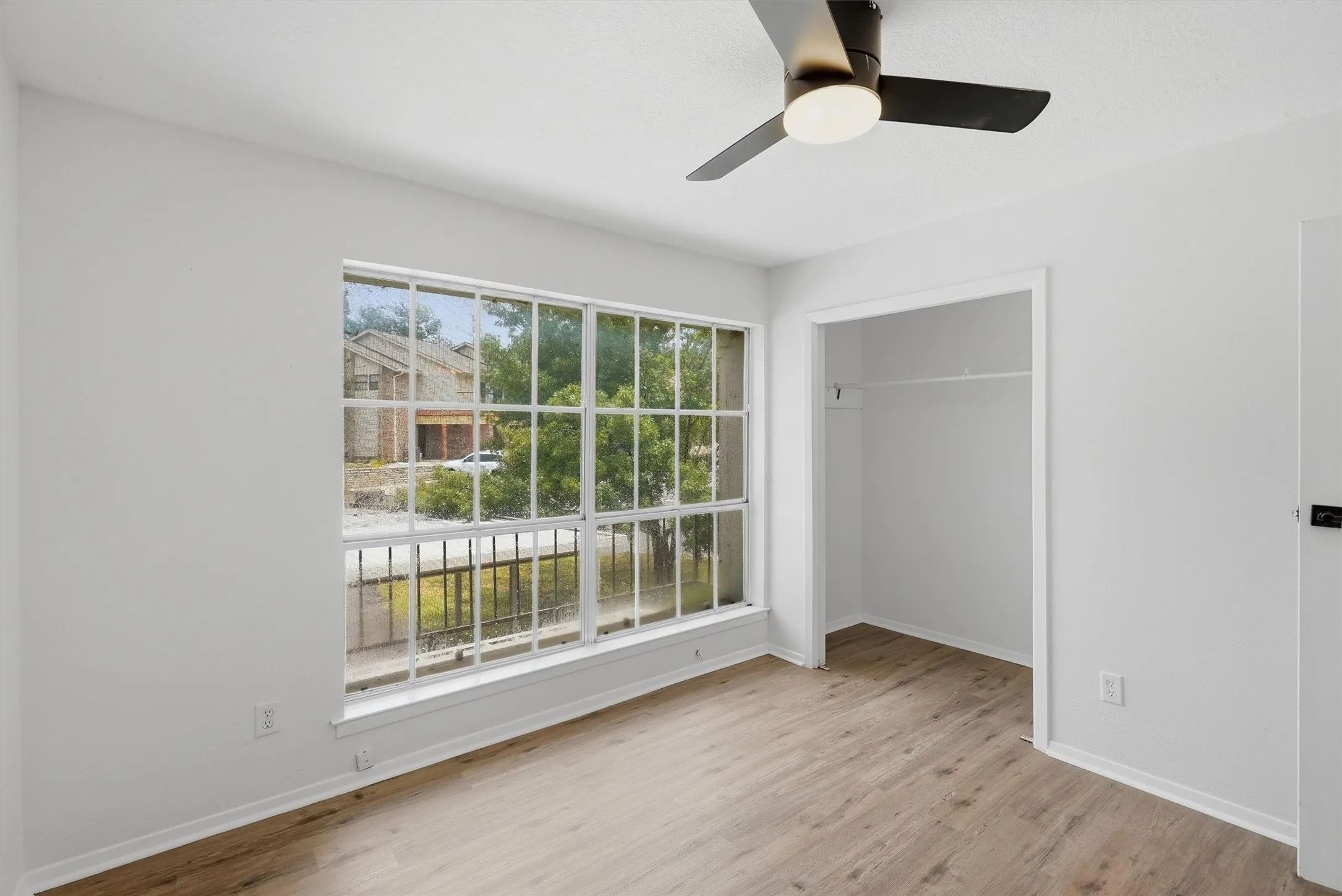 Room with wood-finish flooring, a multi-pane window, and a built-in closet with a hanging rod