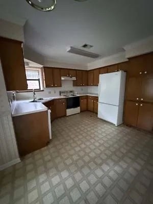 Kitchen featuring wood-finish cabinetry, white countertops, built-in stove, overhead fluorescent lighting, and patterned floor tiling