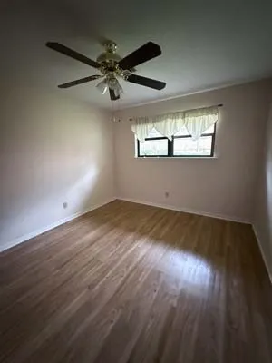 Room featuring wood-finish flooring, a ceiling fan with integrated lighting, and a single window with a valance