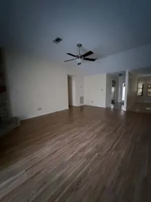 Spacious room featuring wood-finish flooring, light-toned walls, and a ceiling fan with integrated lighting