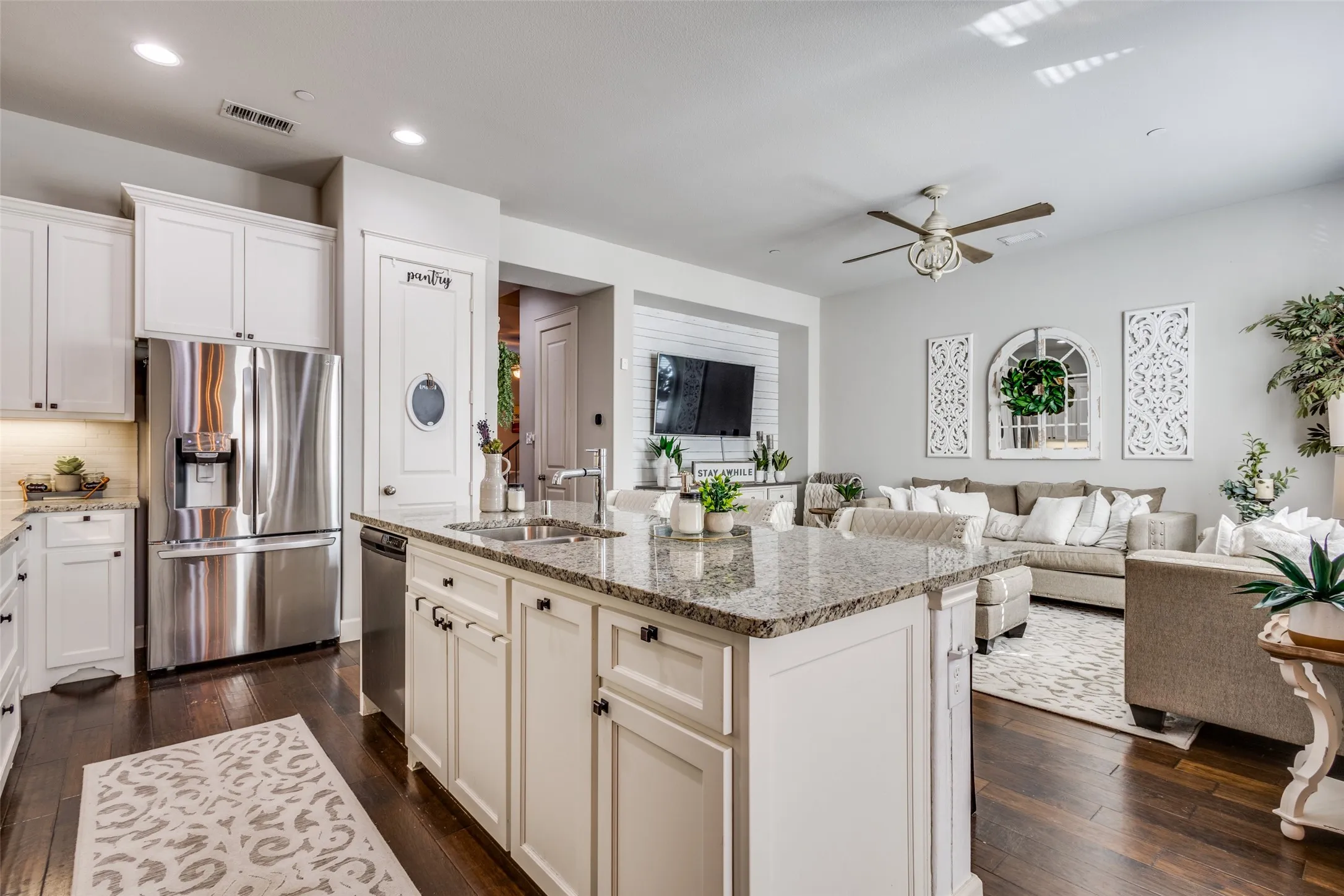 Open-concept kitchen featuring an island with granite countertops, integrated sink, and white cabinetry