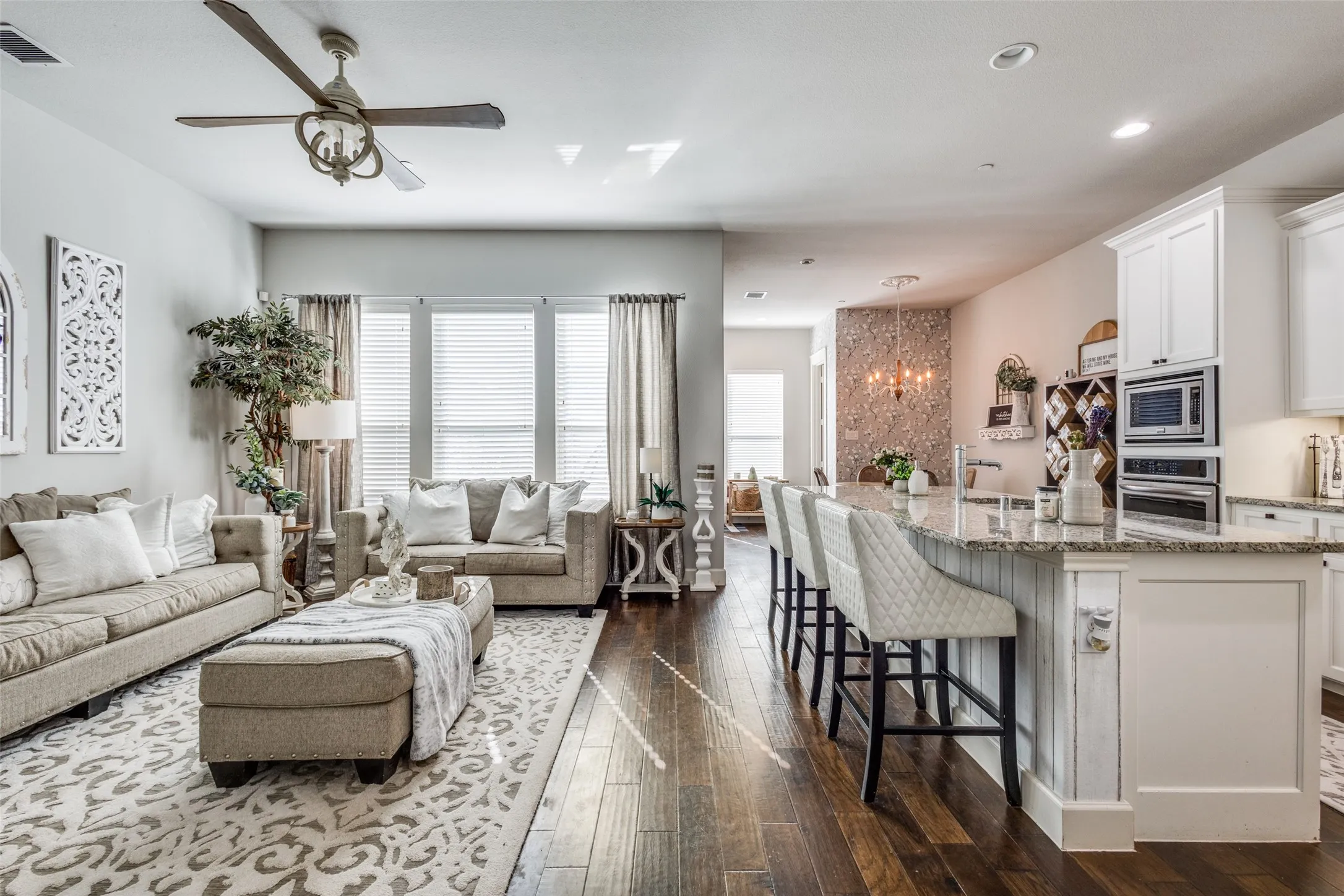 Open-concept living area featuring rich wood-finish flooring, a contemporary ceiling fan, and large windows with blinds