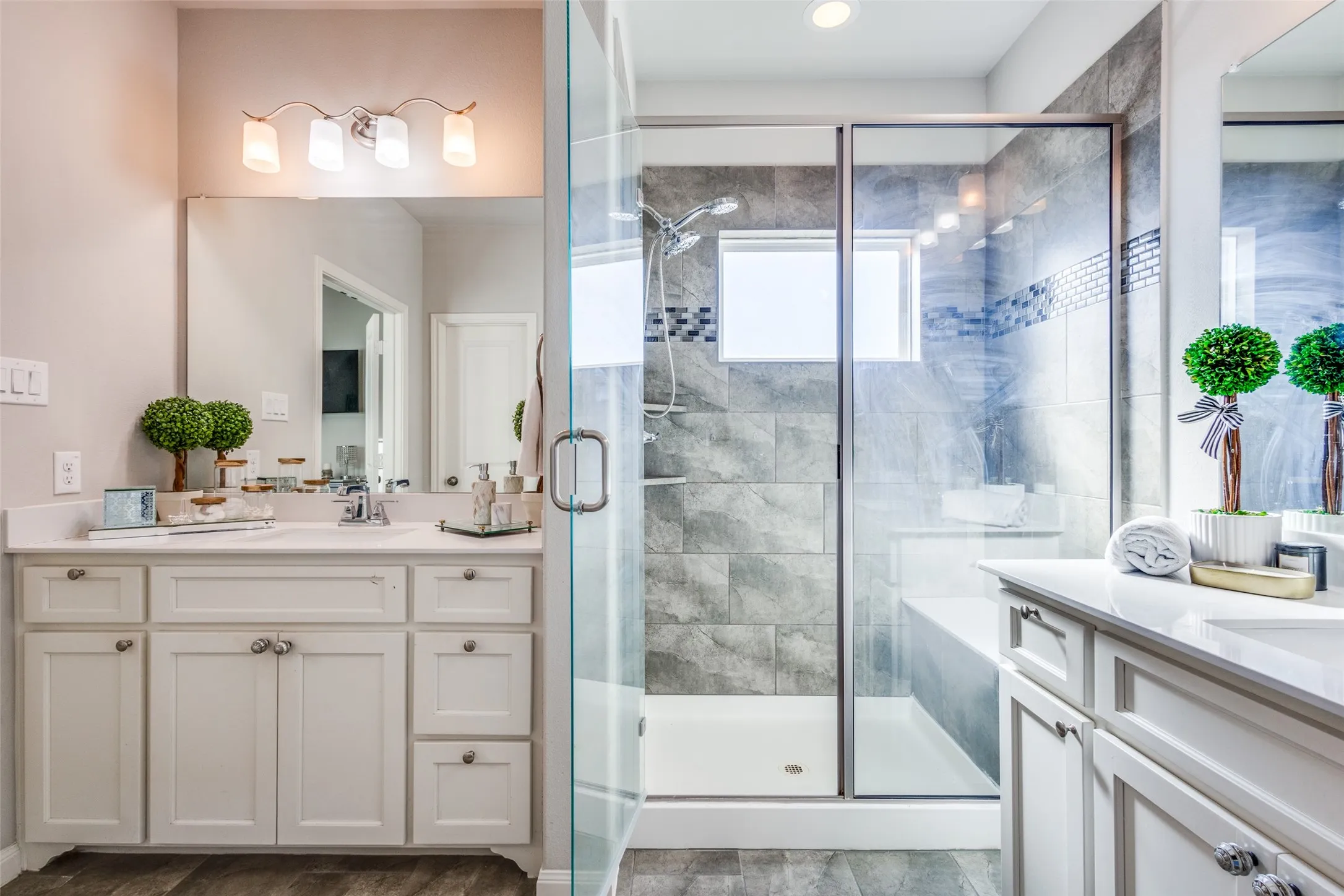 Dual vanity sinks with quartz countertops, a spacious glass-enclosed shower with a built-in bench, gray tile flooring, and decorative tile accents