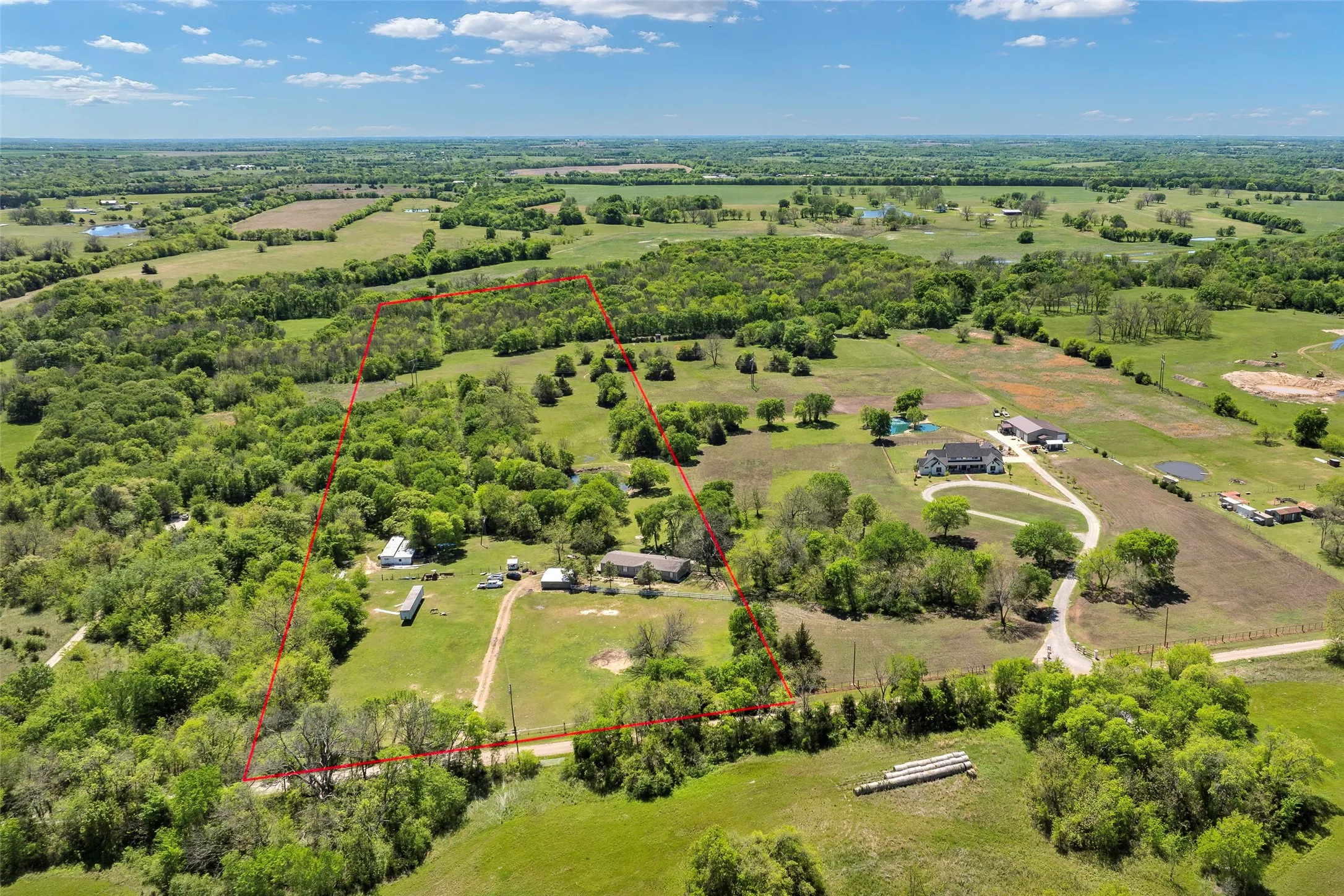 Expansive rural property featuring a large primary residence, multiple secondary structures, and extensive wooded areas