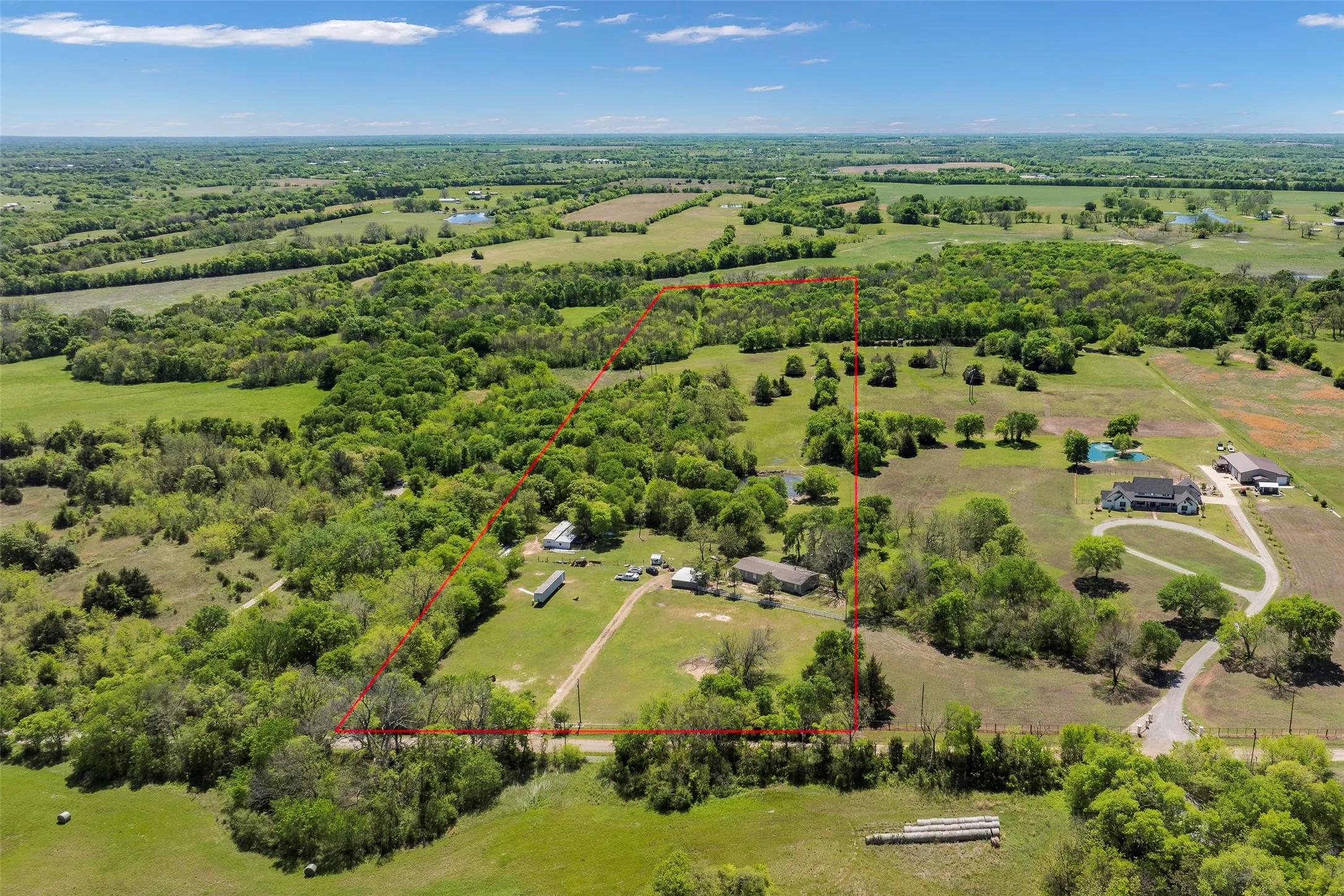 Expansive rural landscape featuring a cleared parcel with multiple structures and wooded areas