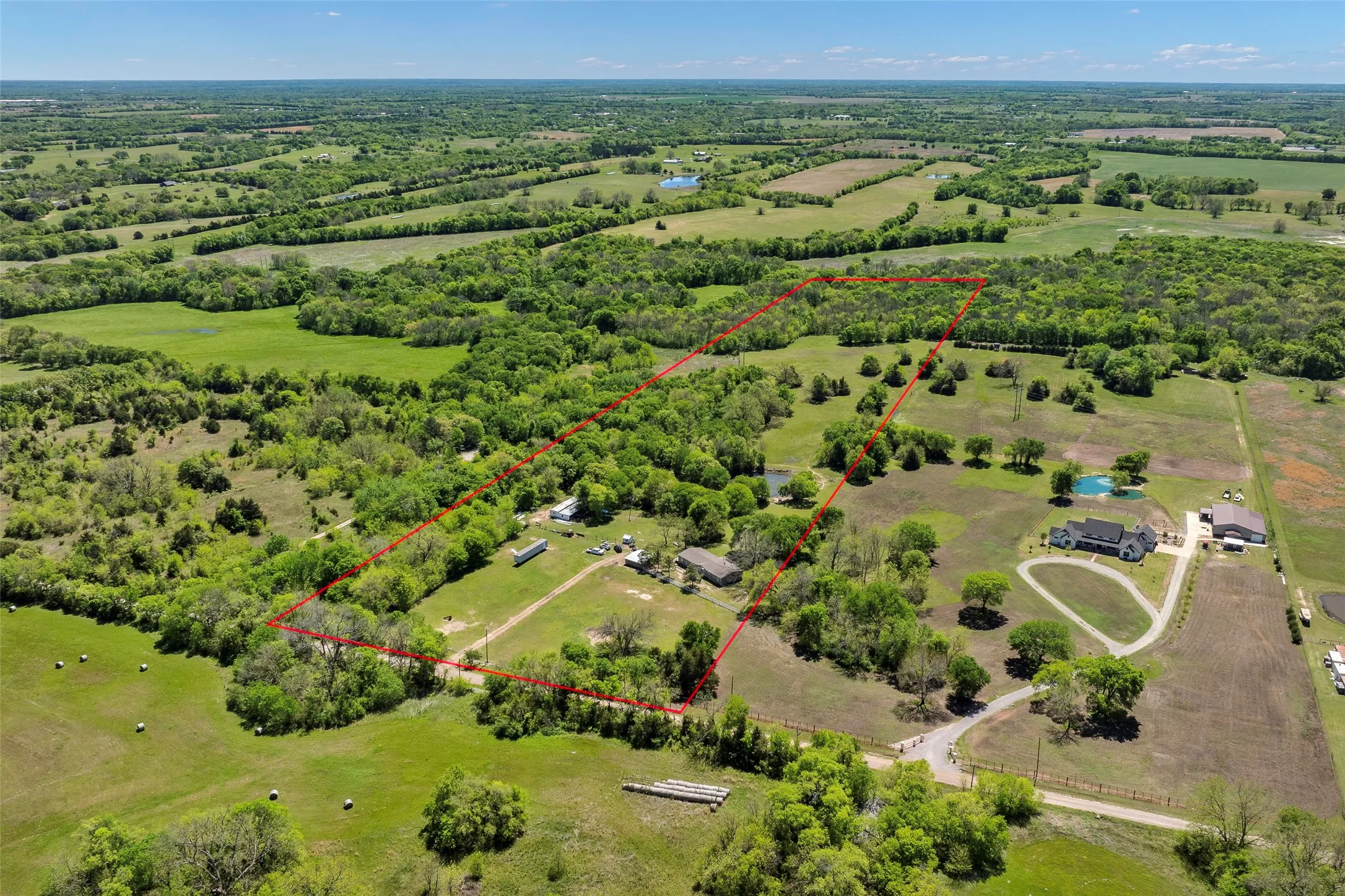 Expansive rural property featuring a defined boundary, multiple structures, a pond, and varying terrain including wooded and open areas
