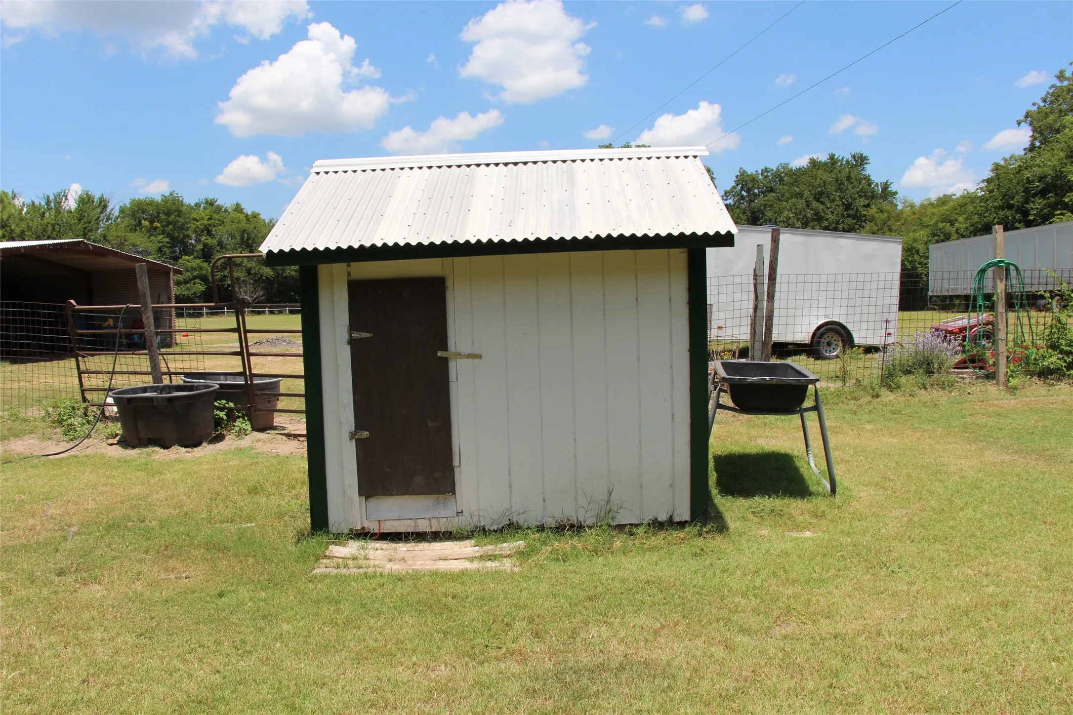White well house with a corrugated metal roof and dark trim, positioned on a grassy area