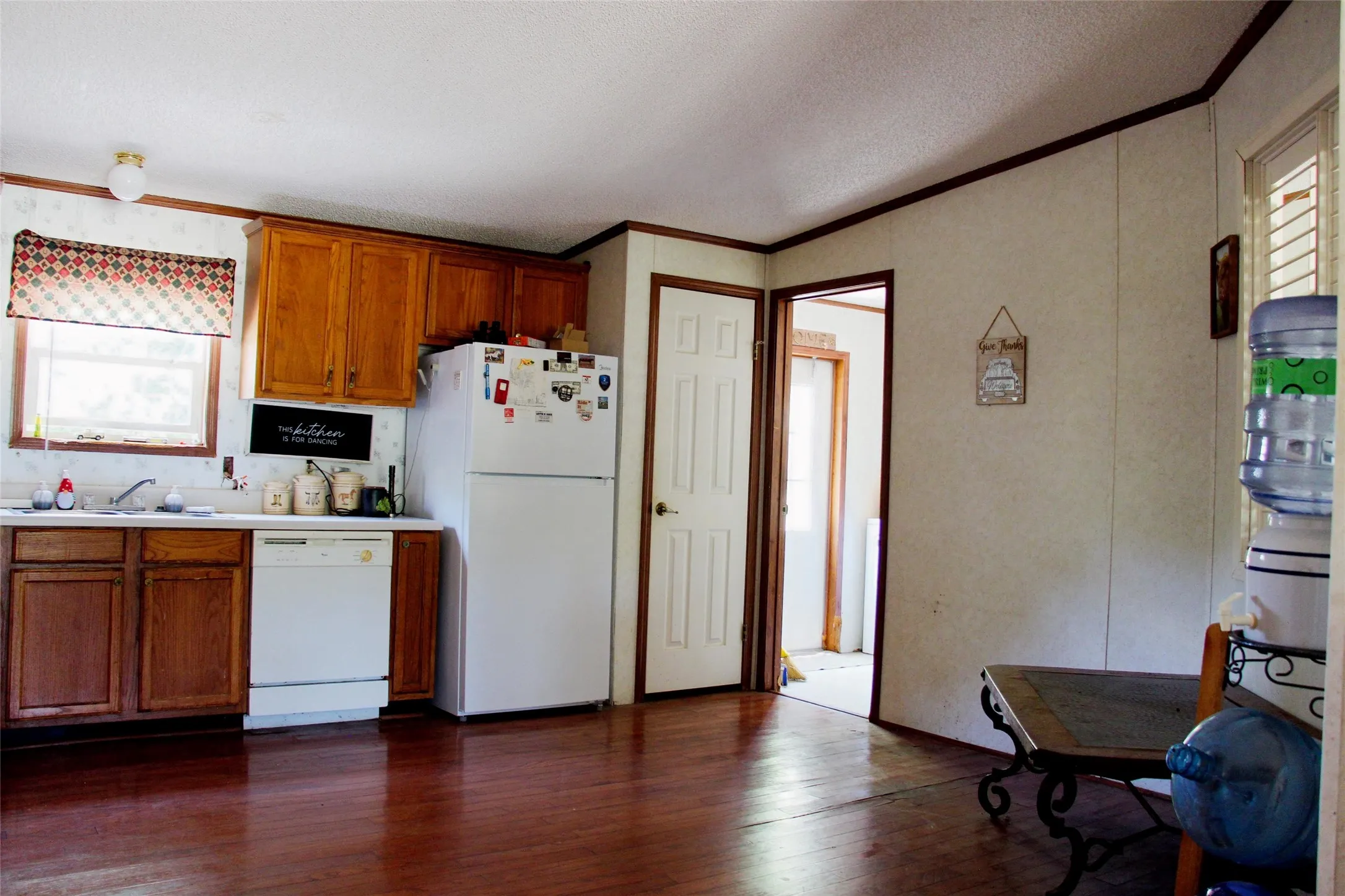 Kitchen featuring wood-finish flooring, white appliances, wood cabinetry, and a window with a patterned valance
