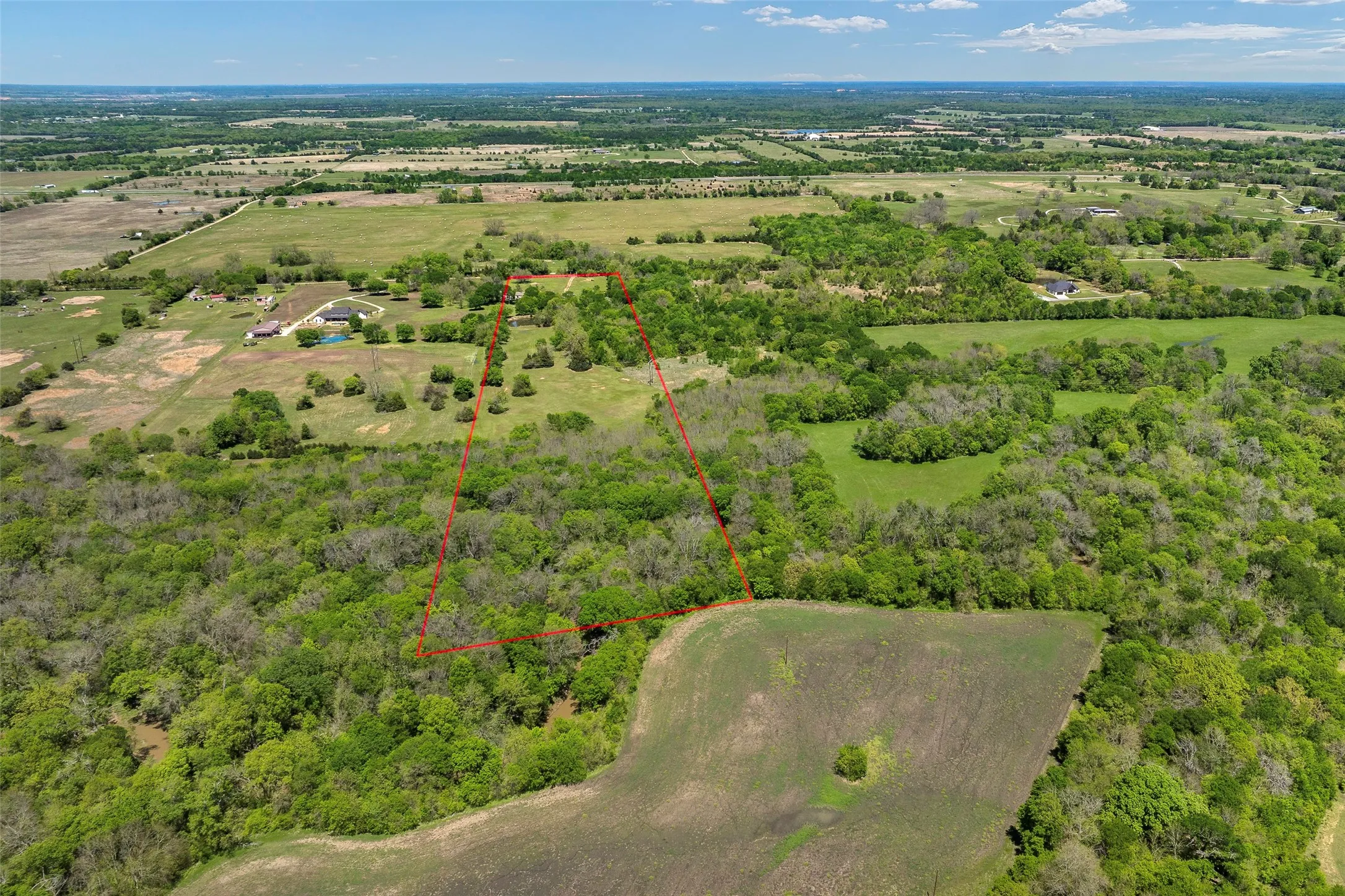 Expansive land parcel featuring a perimeter boundary, mature trees, open grassy areas, and distant agricultural fields