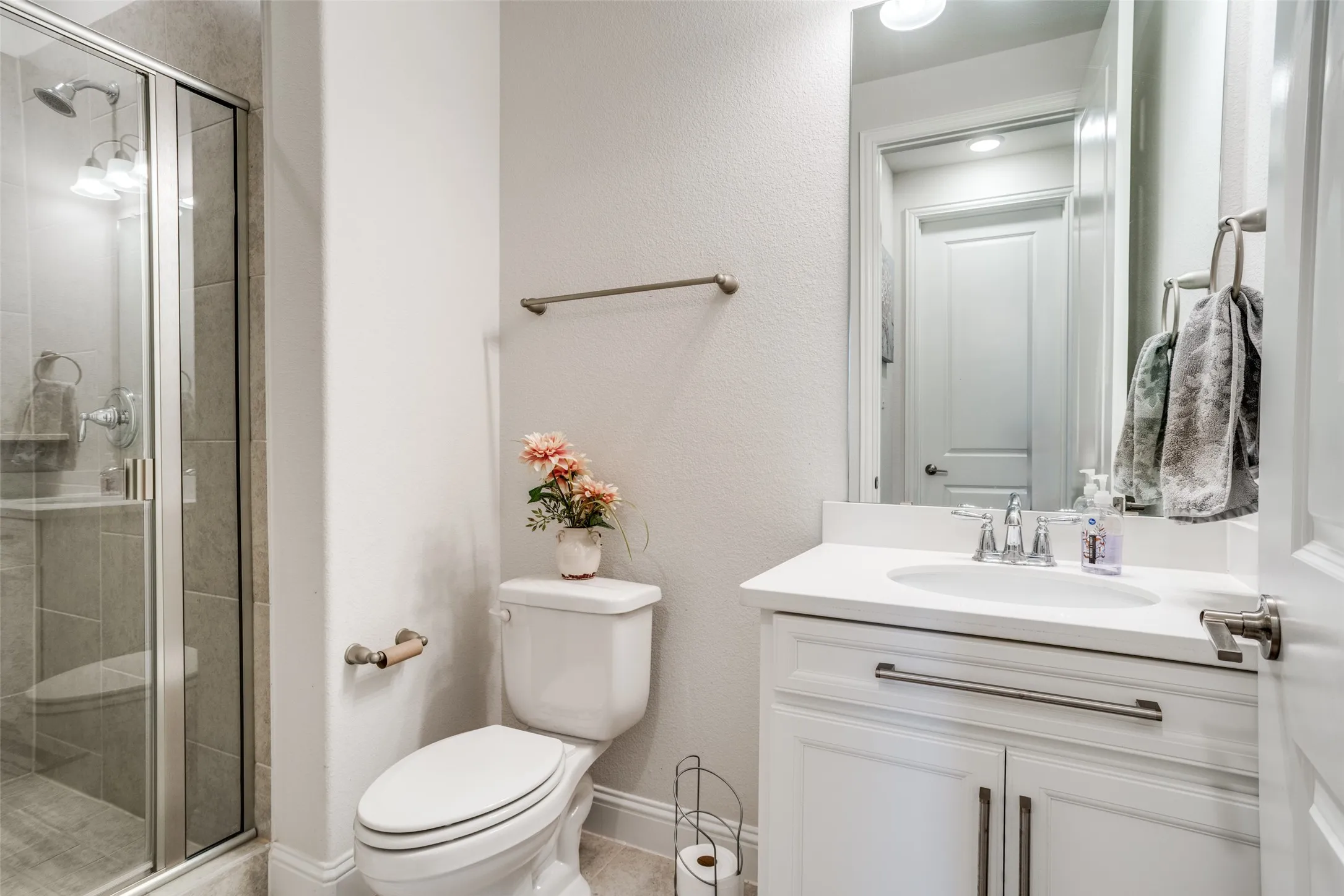 Bathroom featuring a glass-enclosed shower, a white vanity with a single basin sink, a wall-mounted mirror, and a toilet