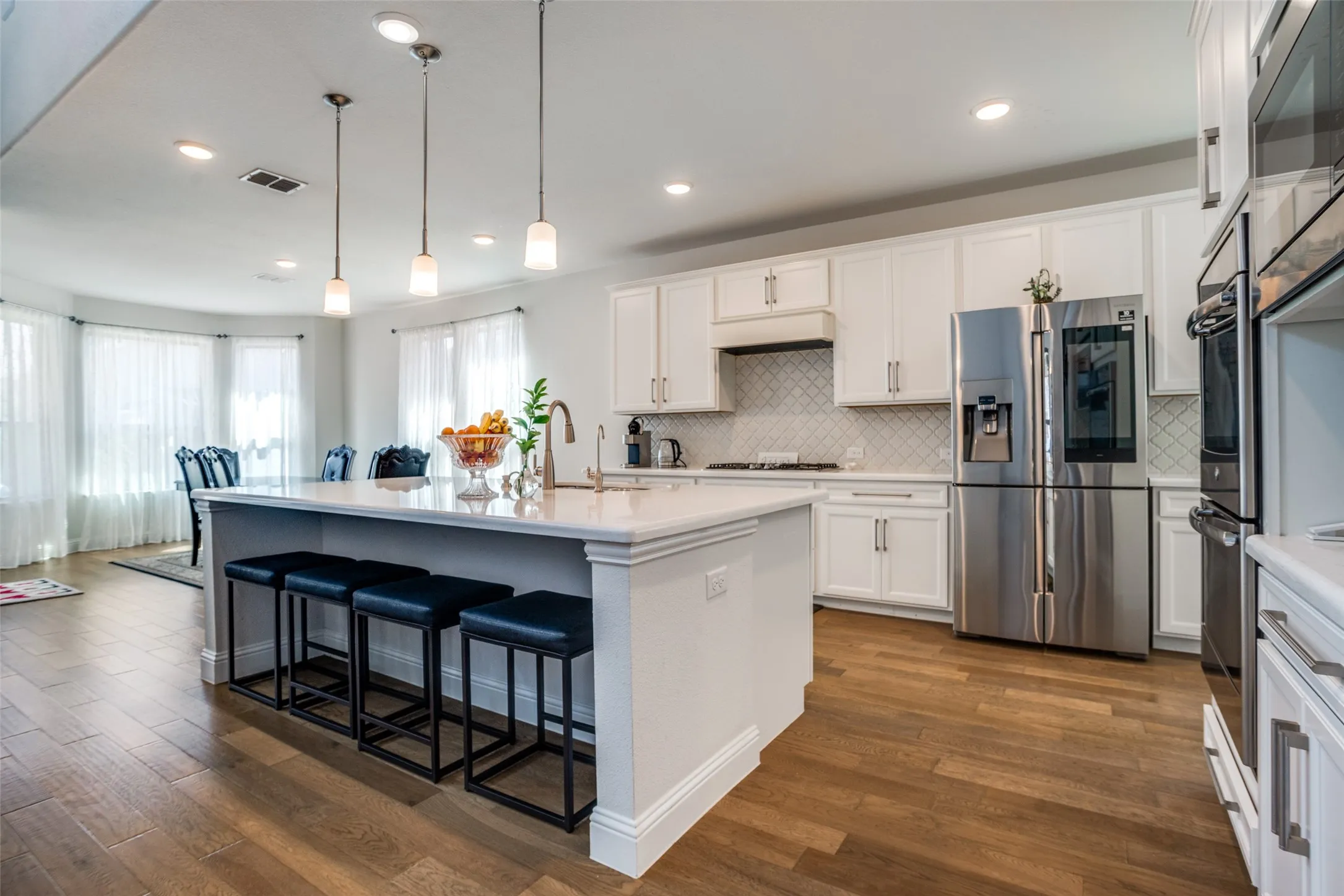 Kitchen featuring white cabinetry, stainless steel appliances, a center island with pendant lighting, wood-finish flooring, and a decorative tile backsplash
