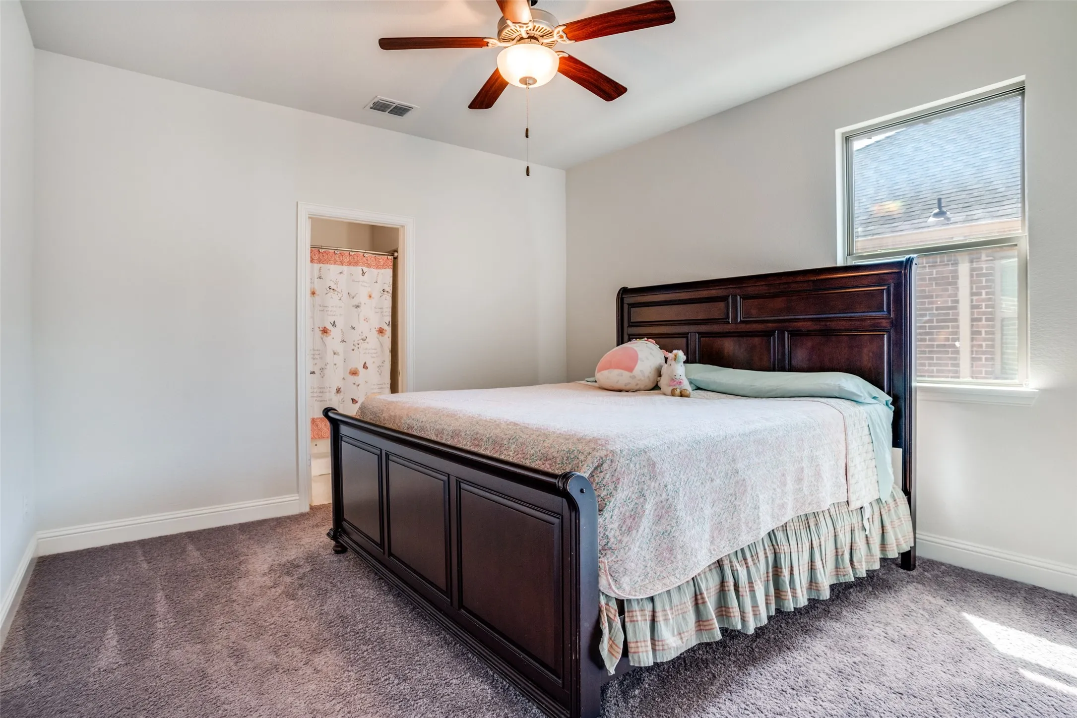 Carpeted room featuring a ceiling fan with integrated lighting, a window with blinds, and an open doorway revealing a shower with a patterned curtain