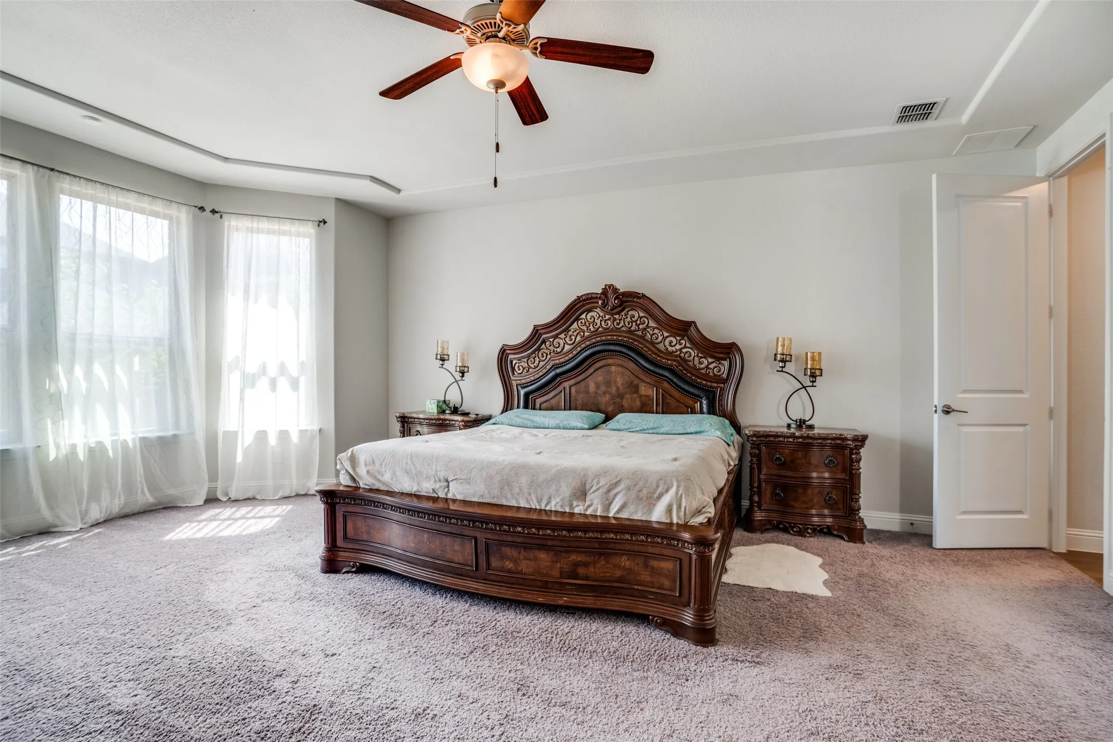 Carpeted bedroom featuring a tray ceiling, ceiling fan with integrated lighting, and multiple windows