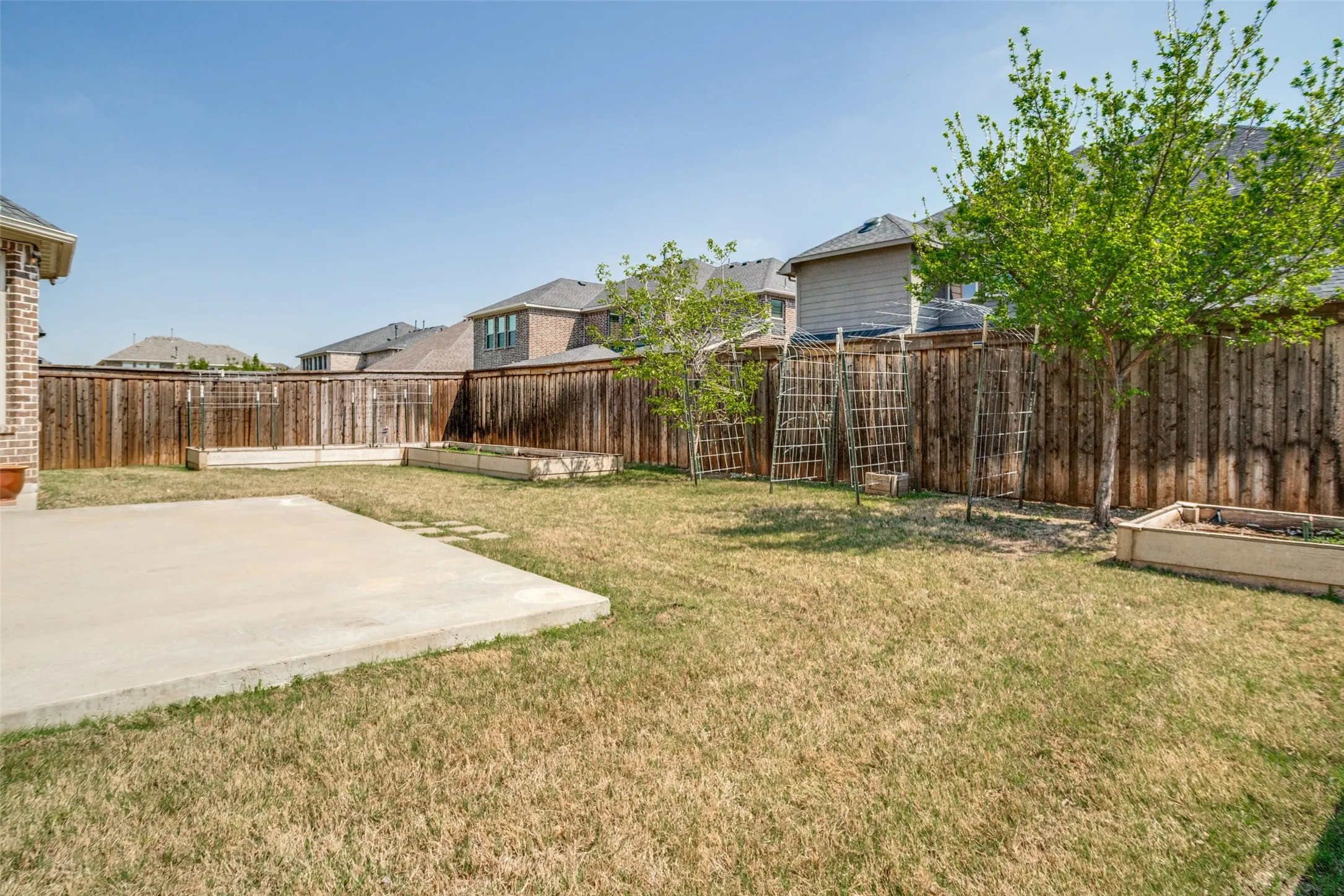 Expansive backyard featuring a concrete patio, wood privacy fencing, two raised garden beds, and mature trees