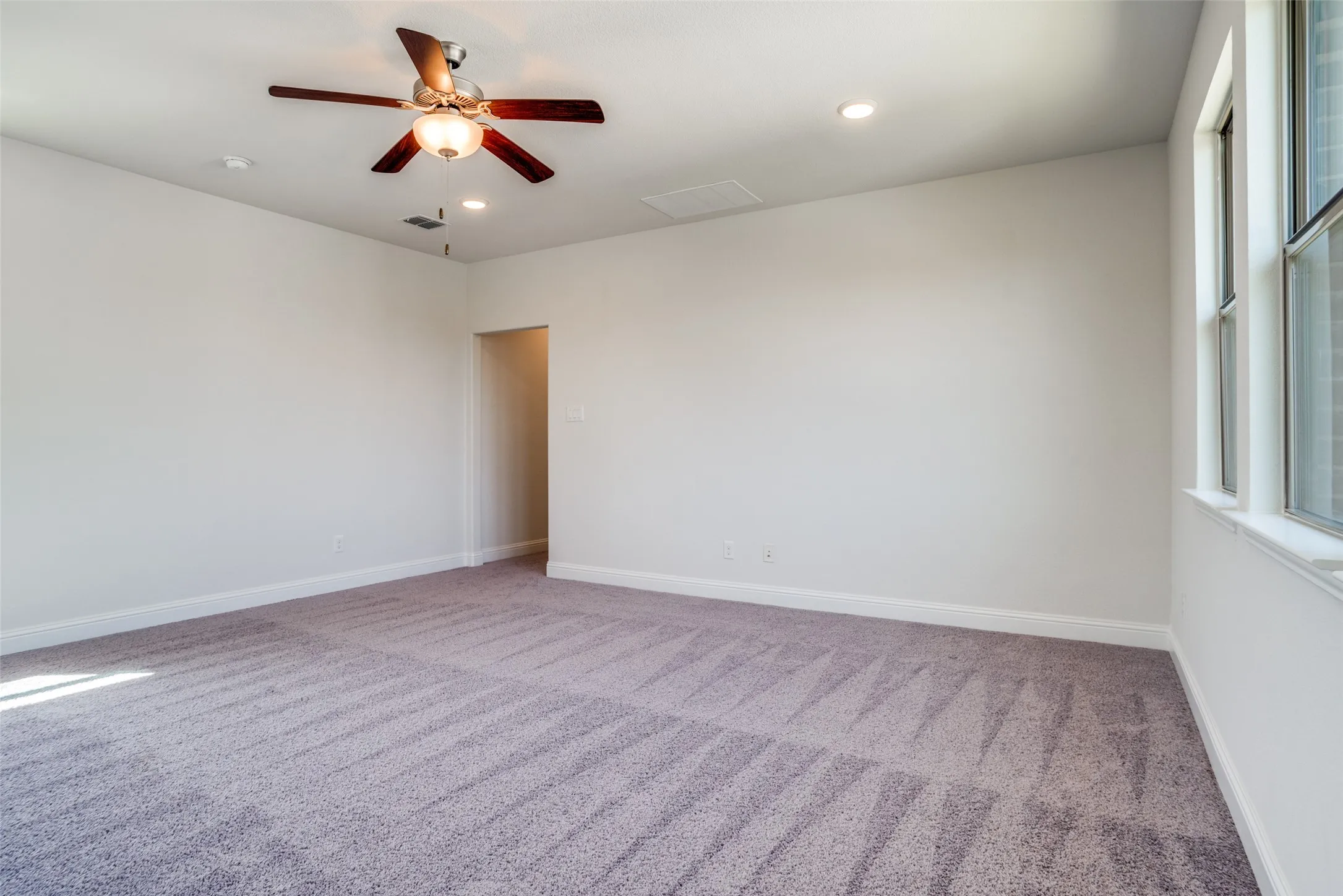 Spacious room featuring light gray carpet, white walls, a ceiling fan with integrated lighting, recessed lighting, and a large window