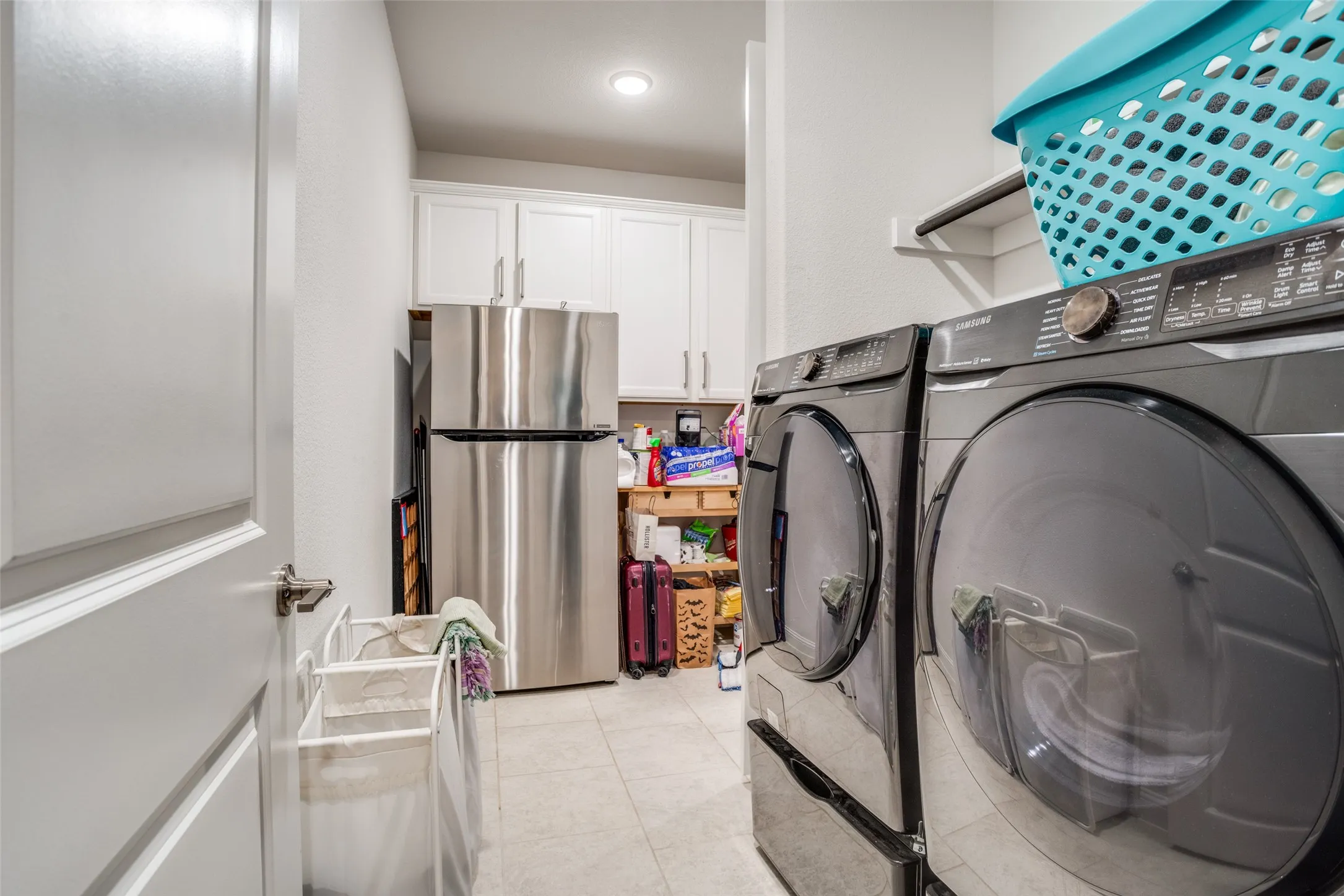 Laundry area featuring light tile flooring, white shaker-style cabinetry, and a built-in shelf