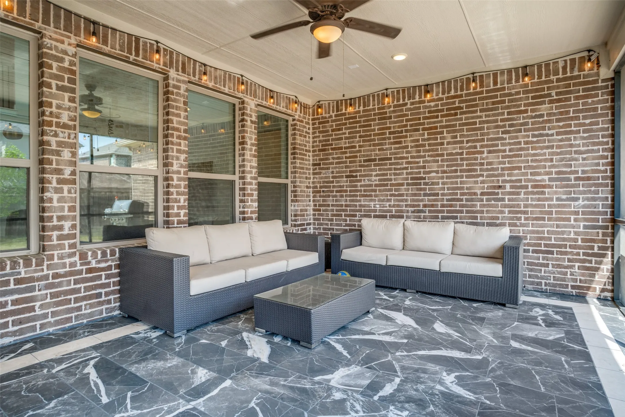 Covered patio featuring a ceiling fan, string lighting, and extensive brickwork