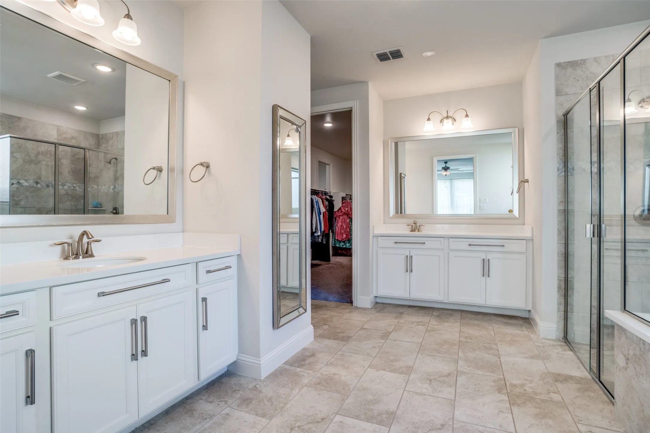 Bathroom featuring dual white cabinetry vanities with stone countertops, framed mirrors, and chrome fixtures