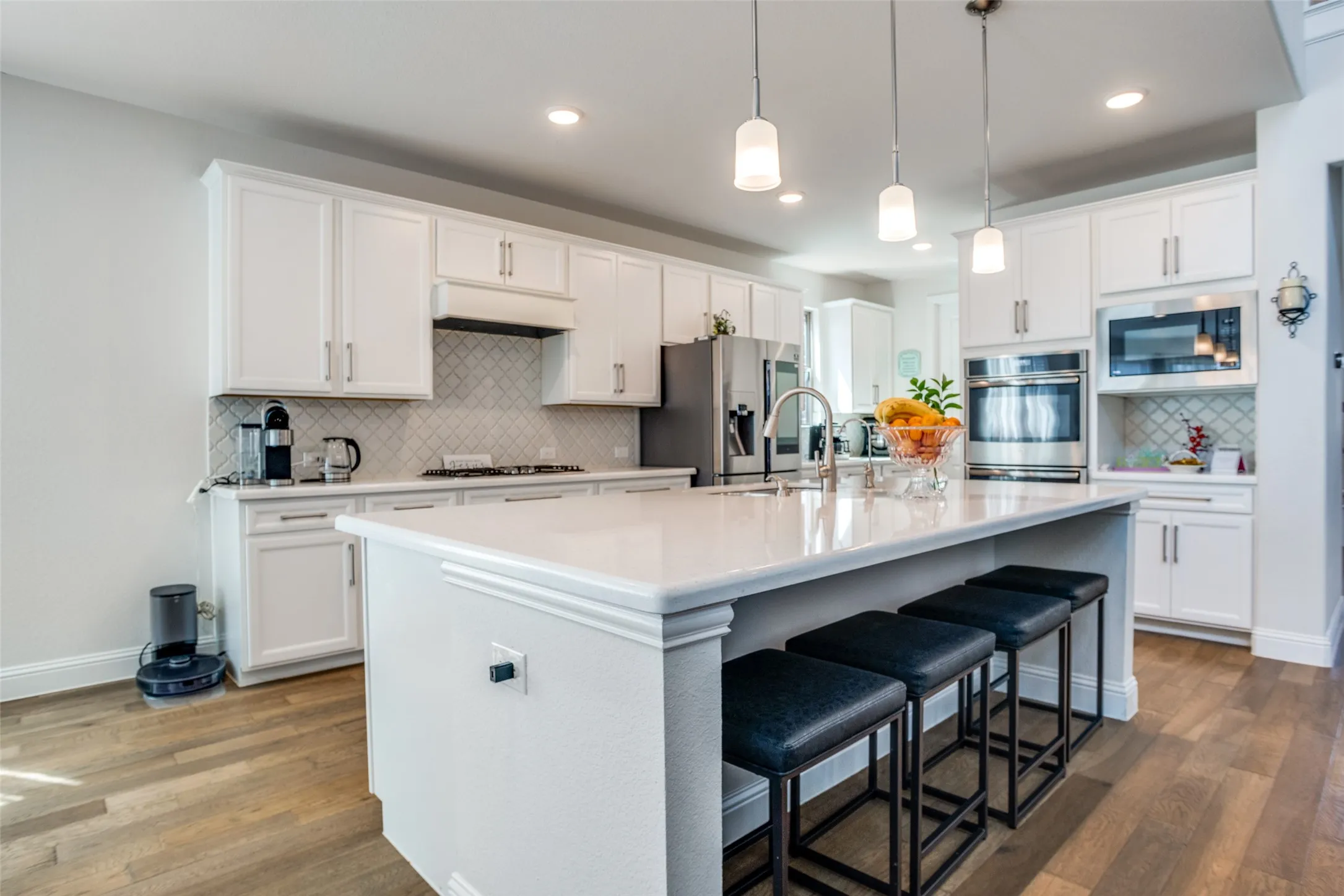 Spacious kitchen featuring white cabinetry, light-toned wood-finish flooring, and a large center island with pendant lighting