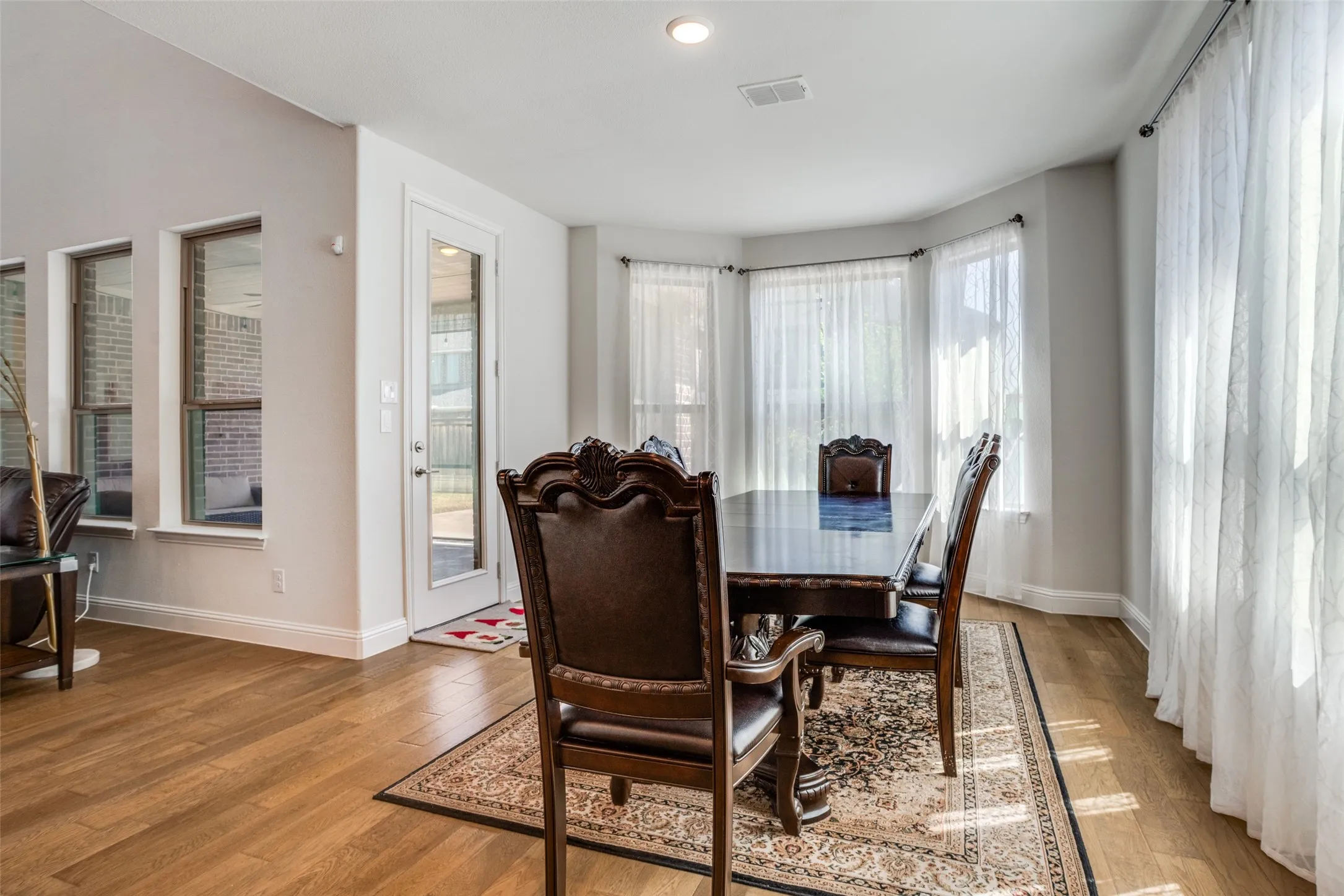 Spacious room featuring wood-finish flooring, a bay window with sheer drapery, recessed lighting, and a glass-paneled exterior door