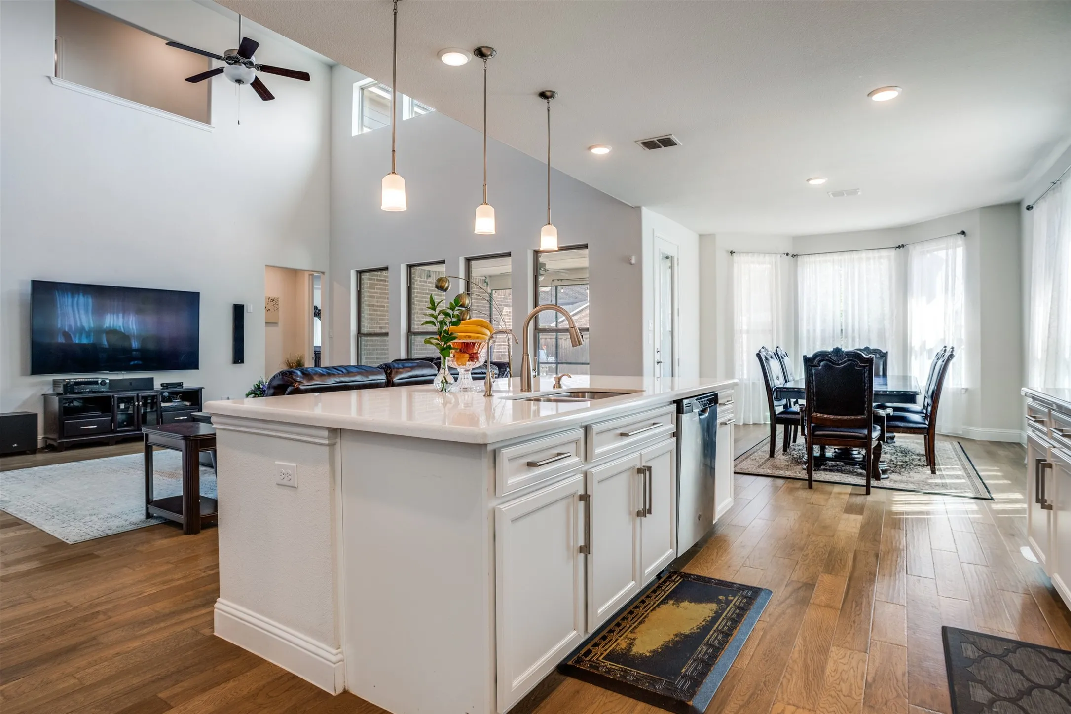 Open-concept living area featuring wood-finish flooring, a kitchen island with pendant lighting, white cabinetry, and high ceilings with a ceiling fan